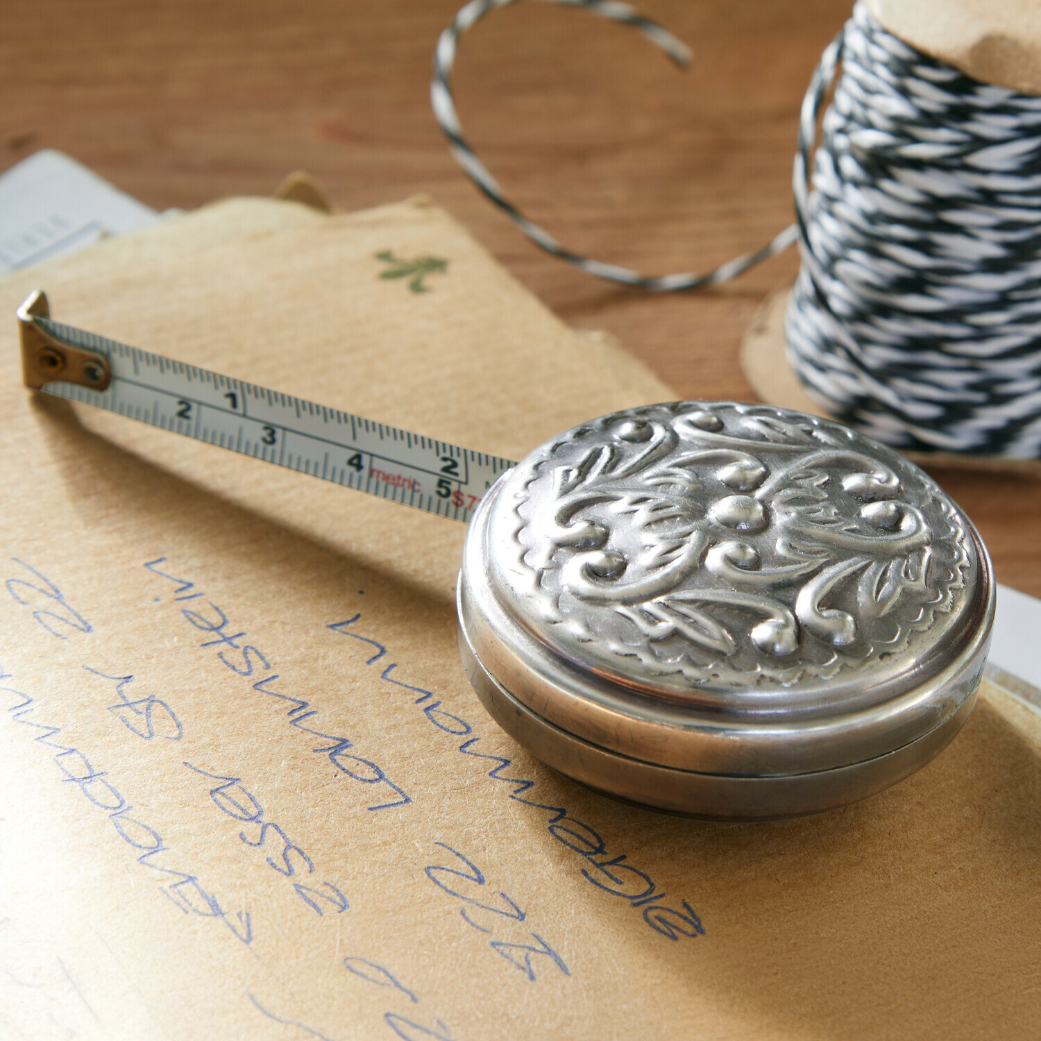 Meetlint Dakota Metalen oprolbare meetlint met plantenmotief op houten tafel naast een klos touw