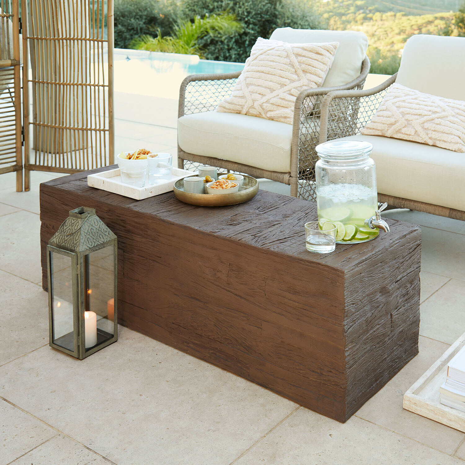 Bruine salontafel met houtstructuur op terras met crèmekussens en limonadekan