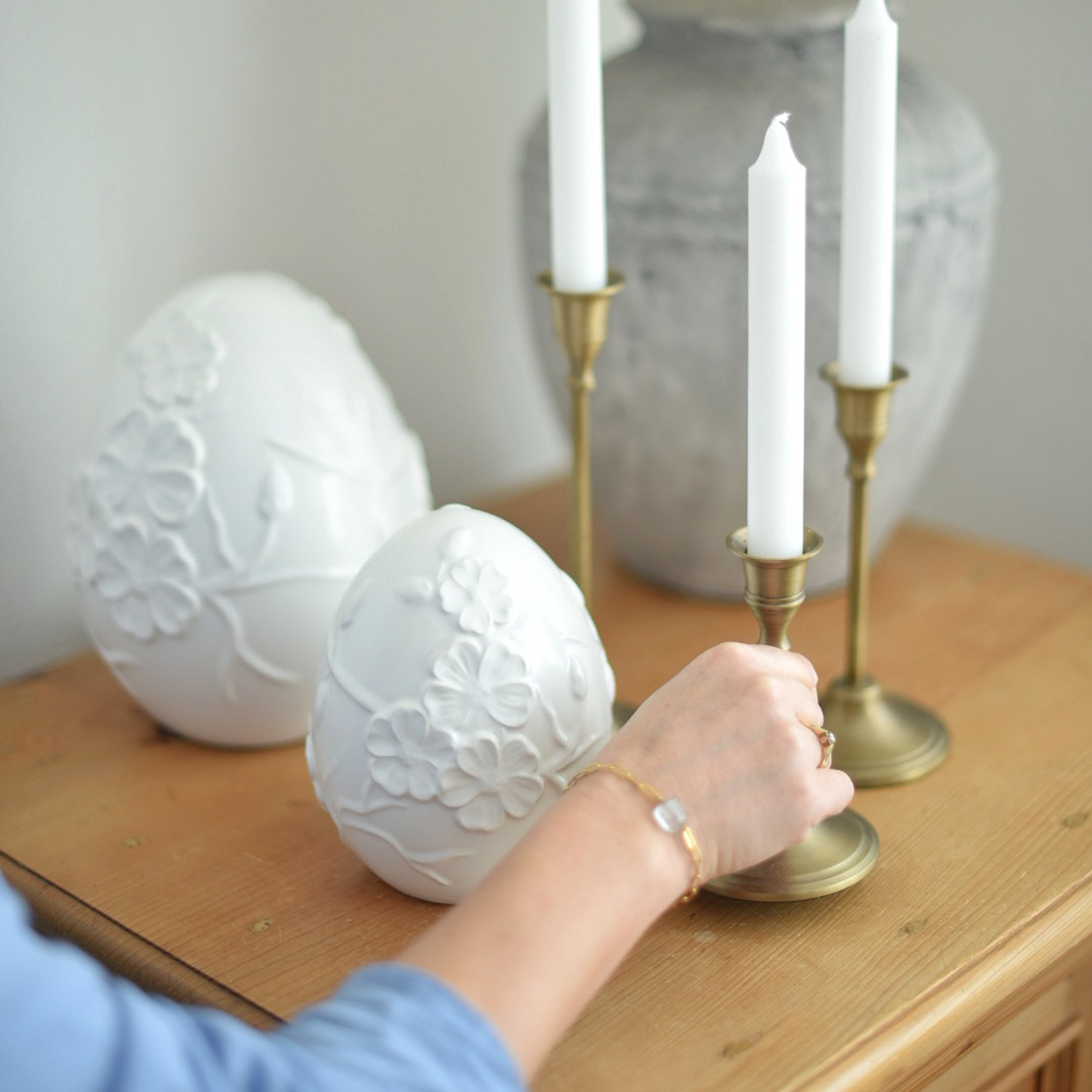 Witte keramische decoratieve eieren met bloemreliëf op houten tafel naast messing kandelaars