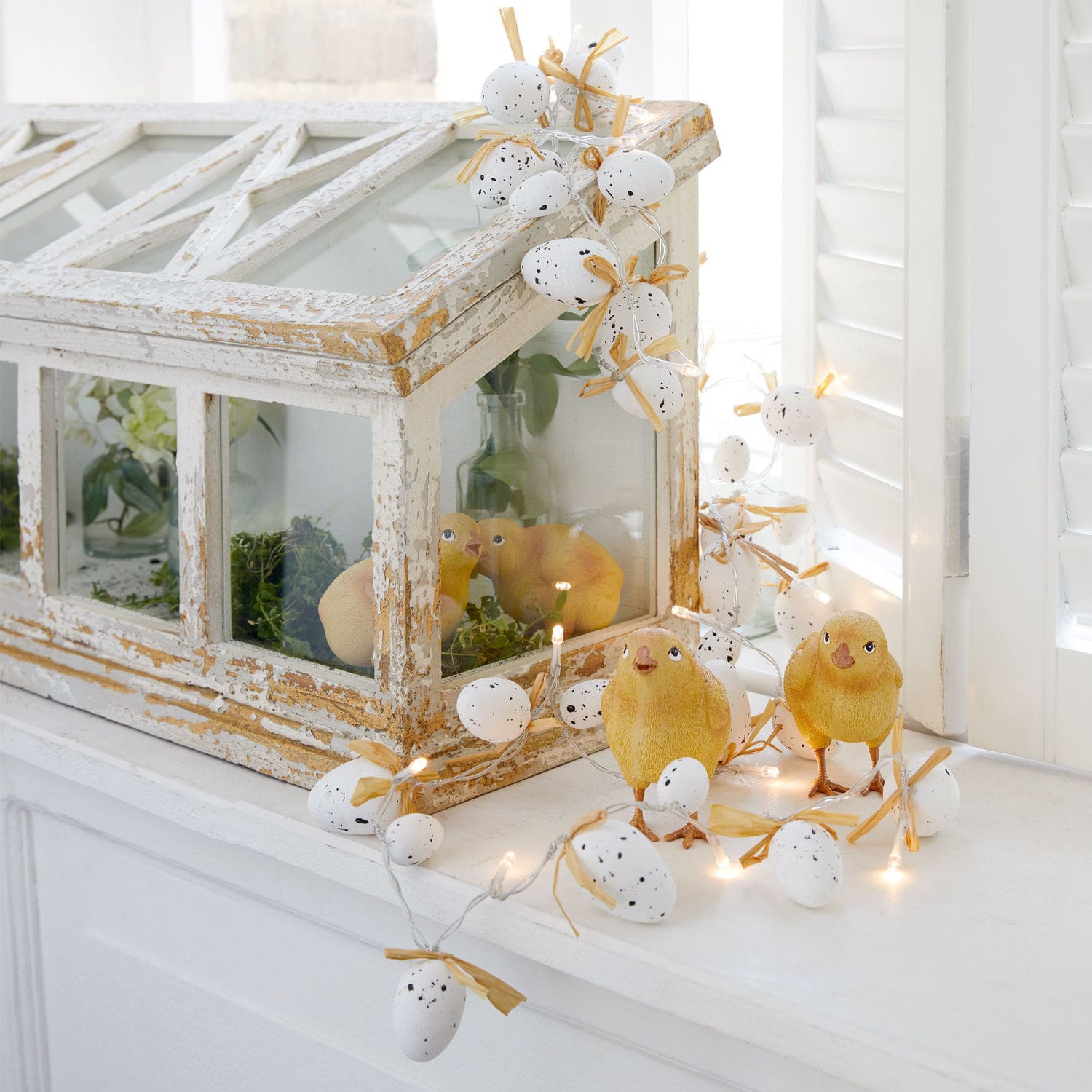 Decoratieve lichtslinger met witte eieren en gele kuikens op een witte vensterbank