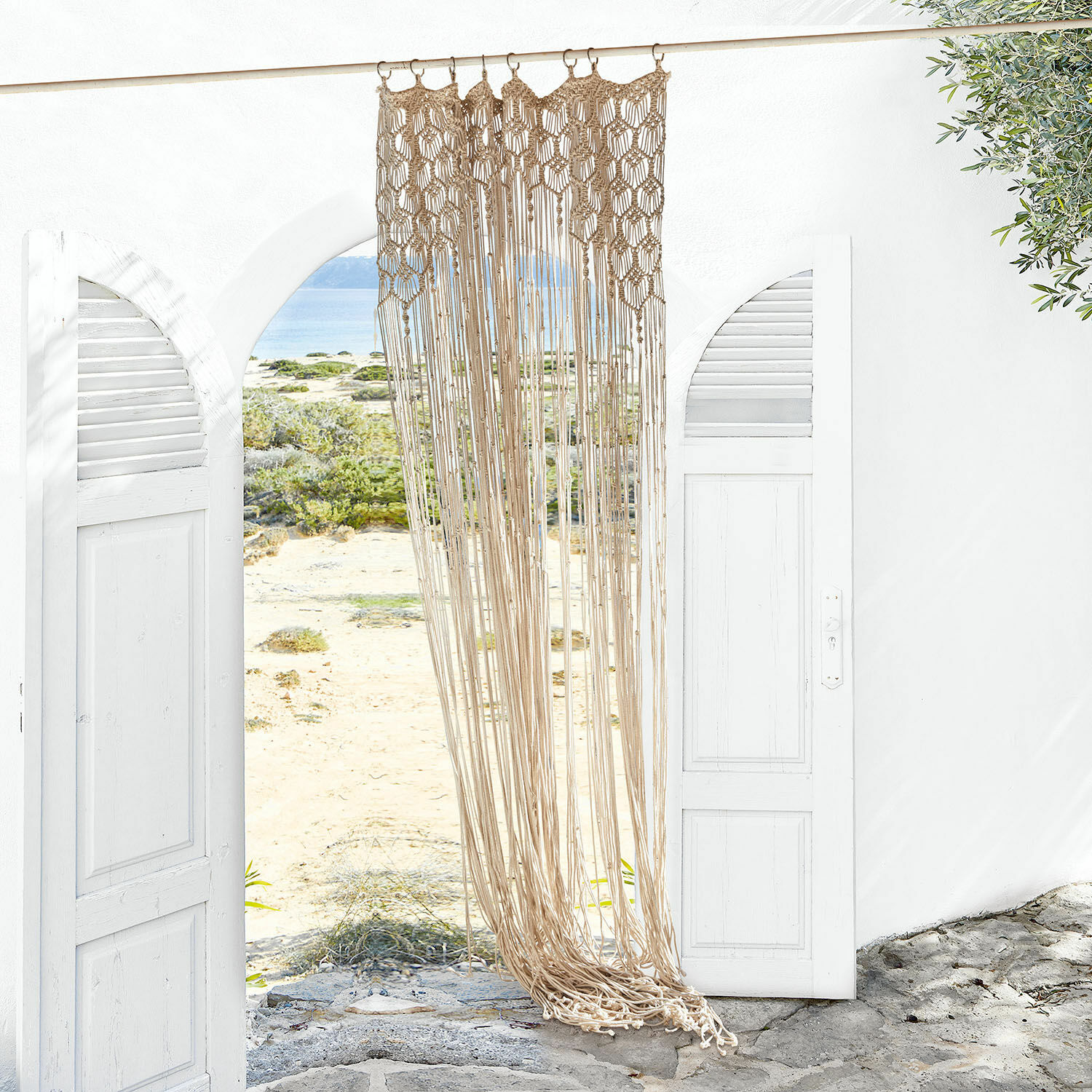 Gordijn Manville Beige katoenen macramé hangend in een witte open ingang met uitzicht op strand en zee
