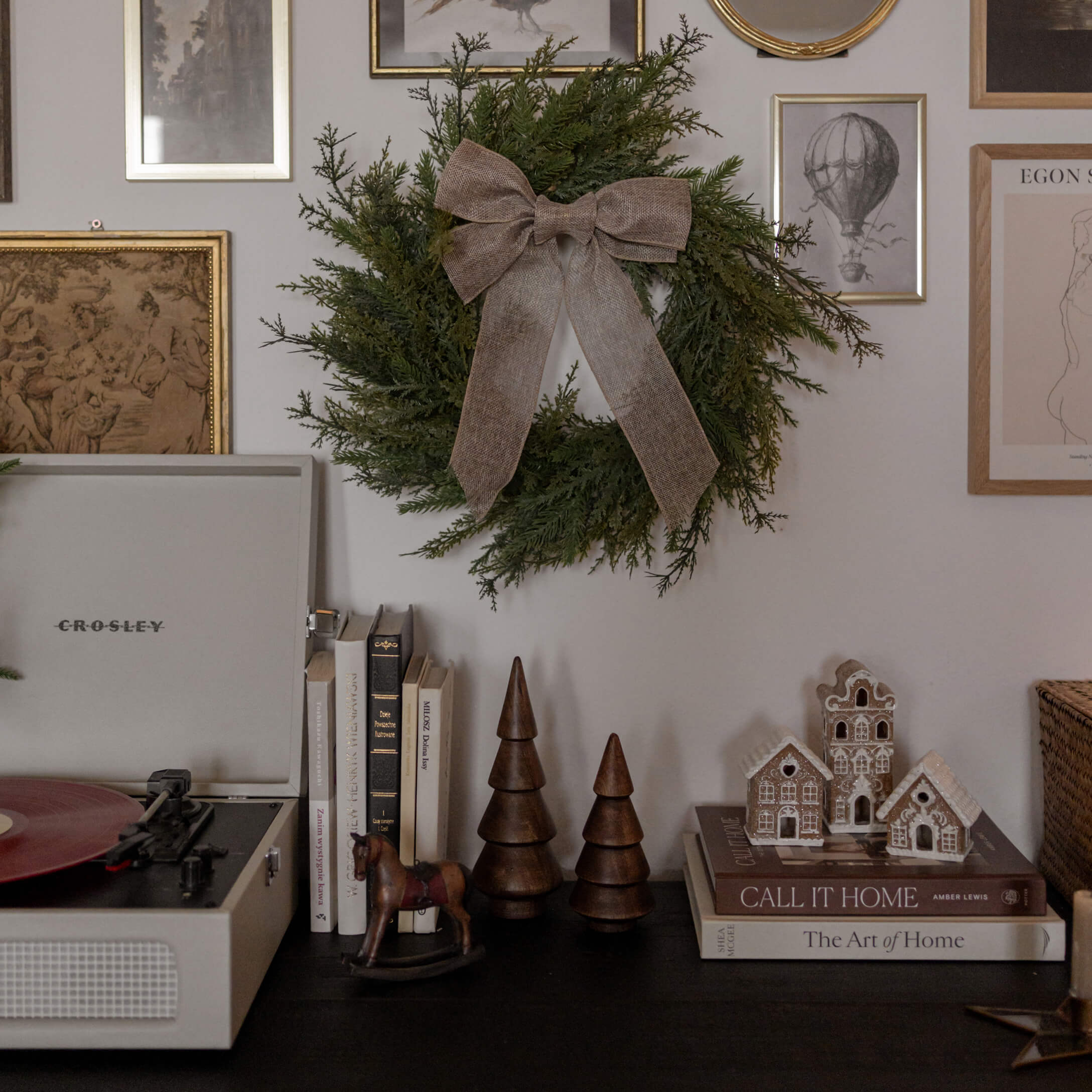 Groene decoratieve krans met bruine strik aan muur boven zwarte tafel met boeken en houten figuren