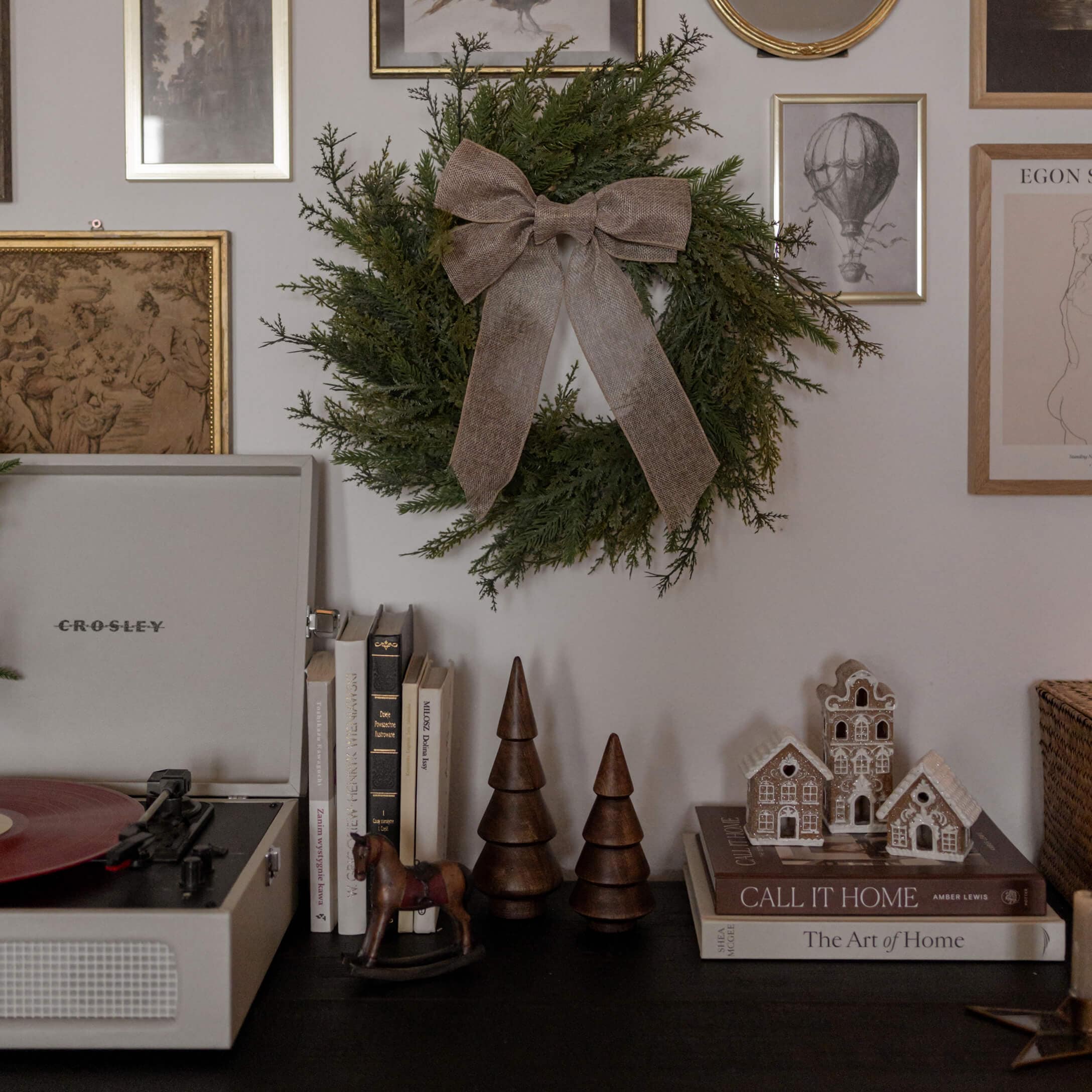 Groene decoratieve krans met bruine strik aan muur boven zwarte tafel met boeken en houten figuren