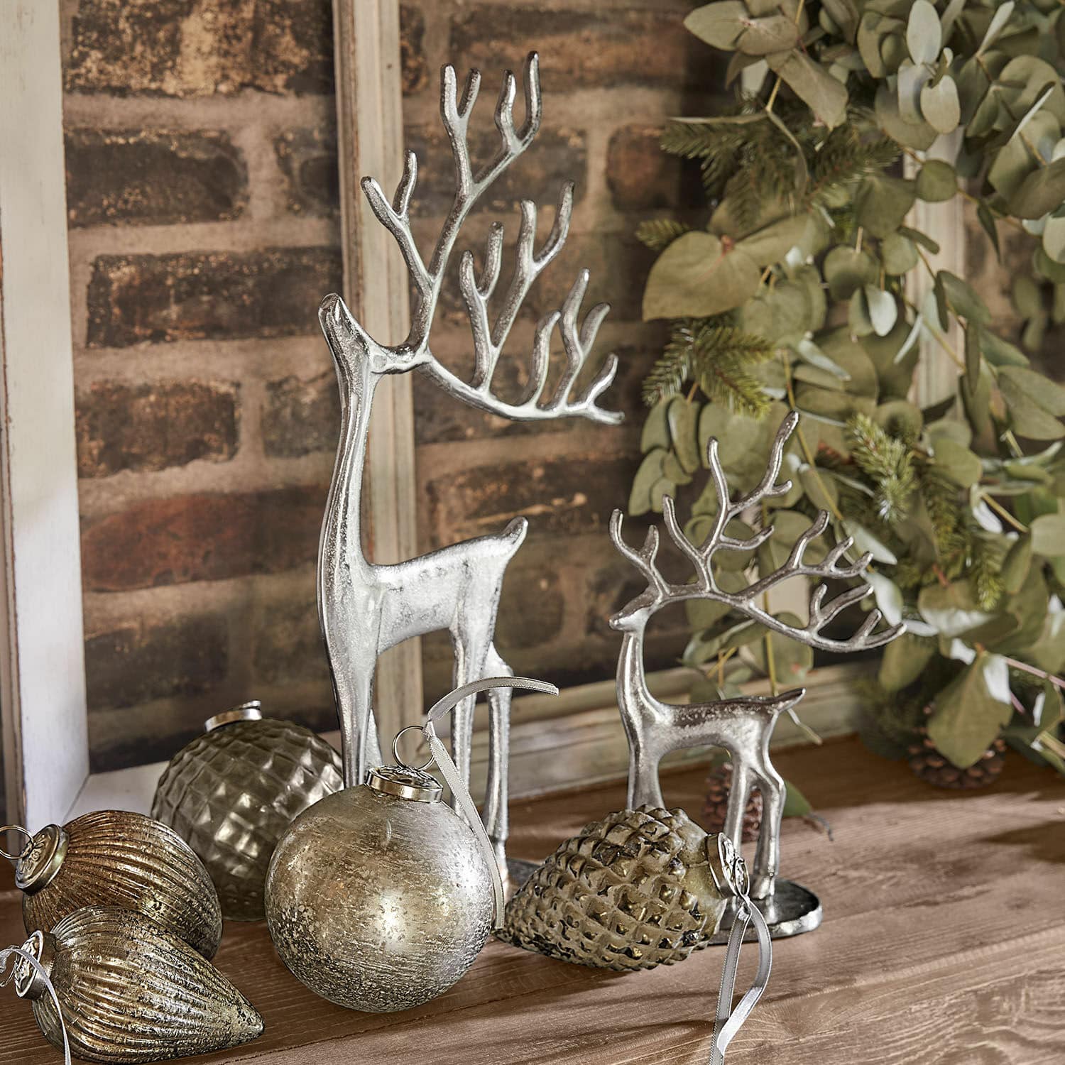 Decoratierendier set van 2 Zerlay Zilveren rendierfiguren en kerstdecoraties op houten tafel met groene takken erachter