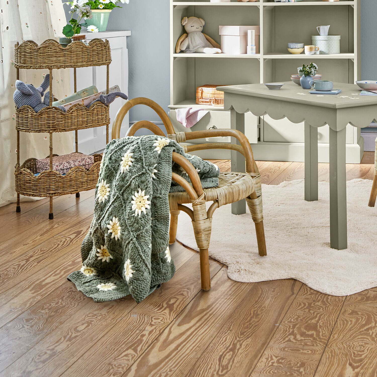 Kinderstoel Tinytreasure Grijze gebreide deken met witte bloemen op rotan stoel in lichte kinderkamer met houten vloer