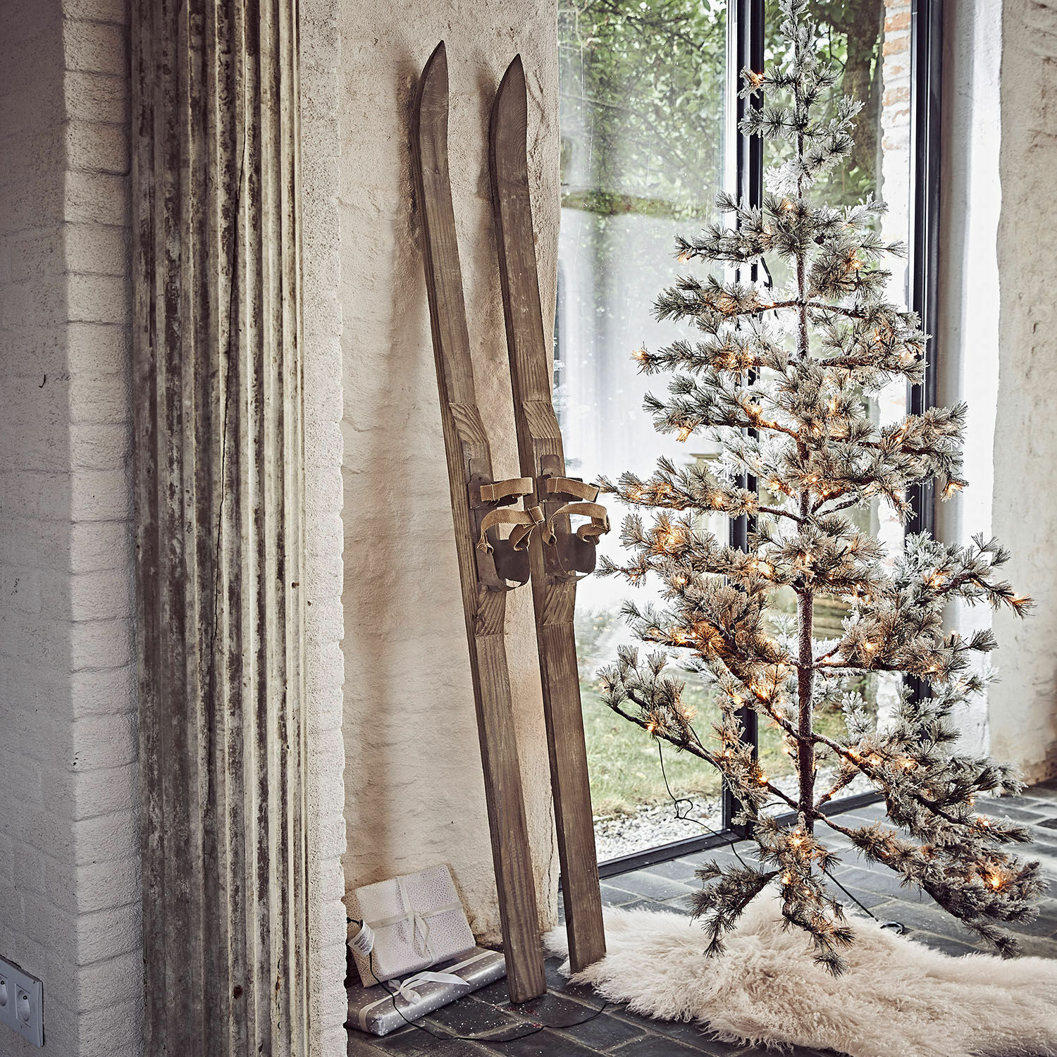 Vintage houten ski's naast verlichte kunstkerstboom op wit vloerkleed
