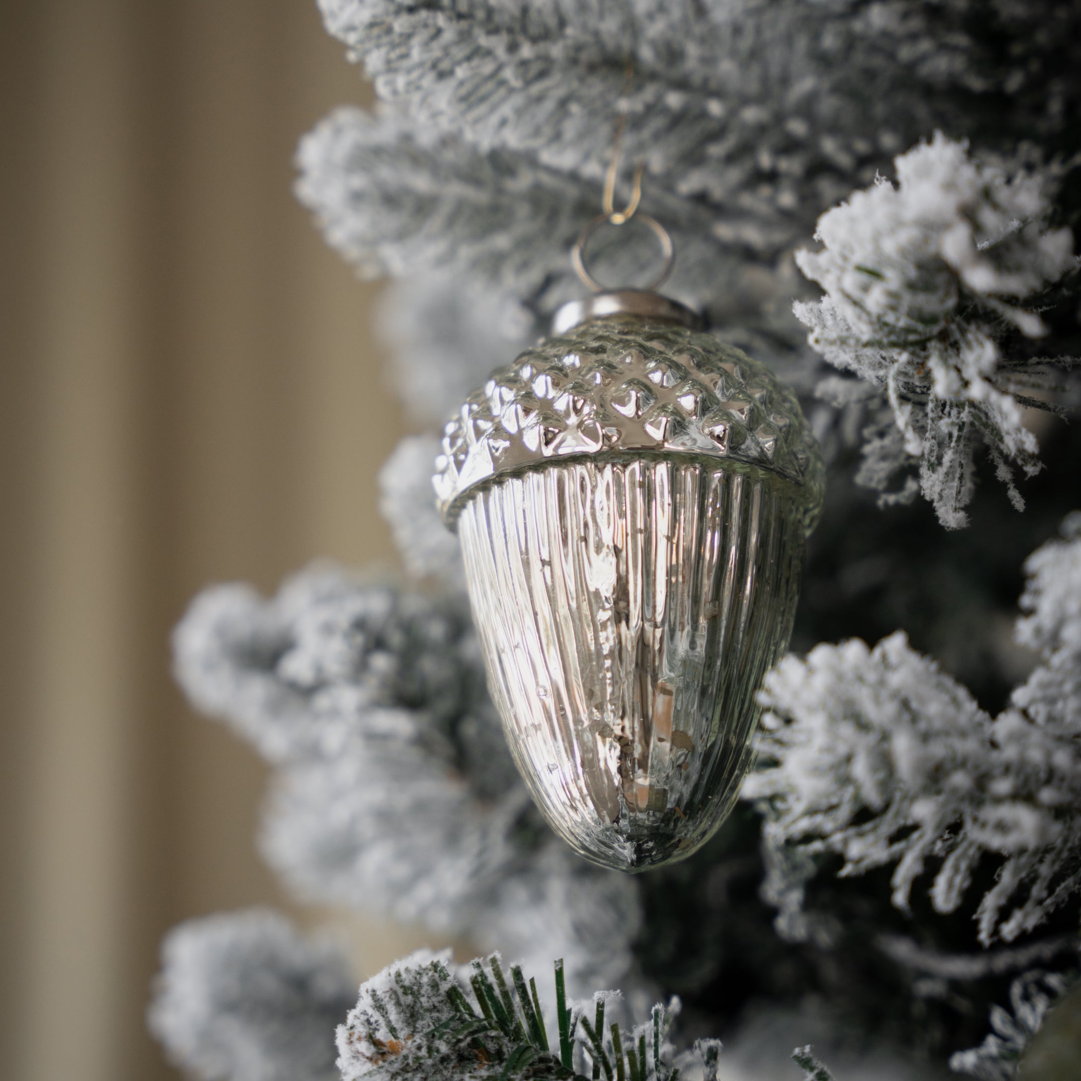 Zilveren eikelvormige kerstbal aan besneeuwde dennentak voor winterse feestdecoratie