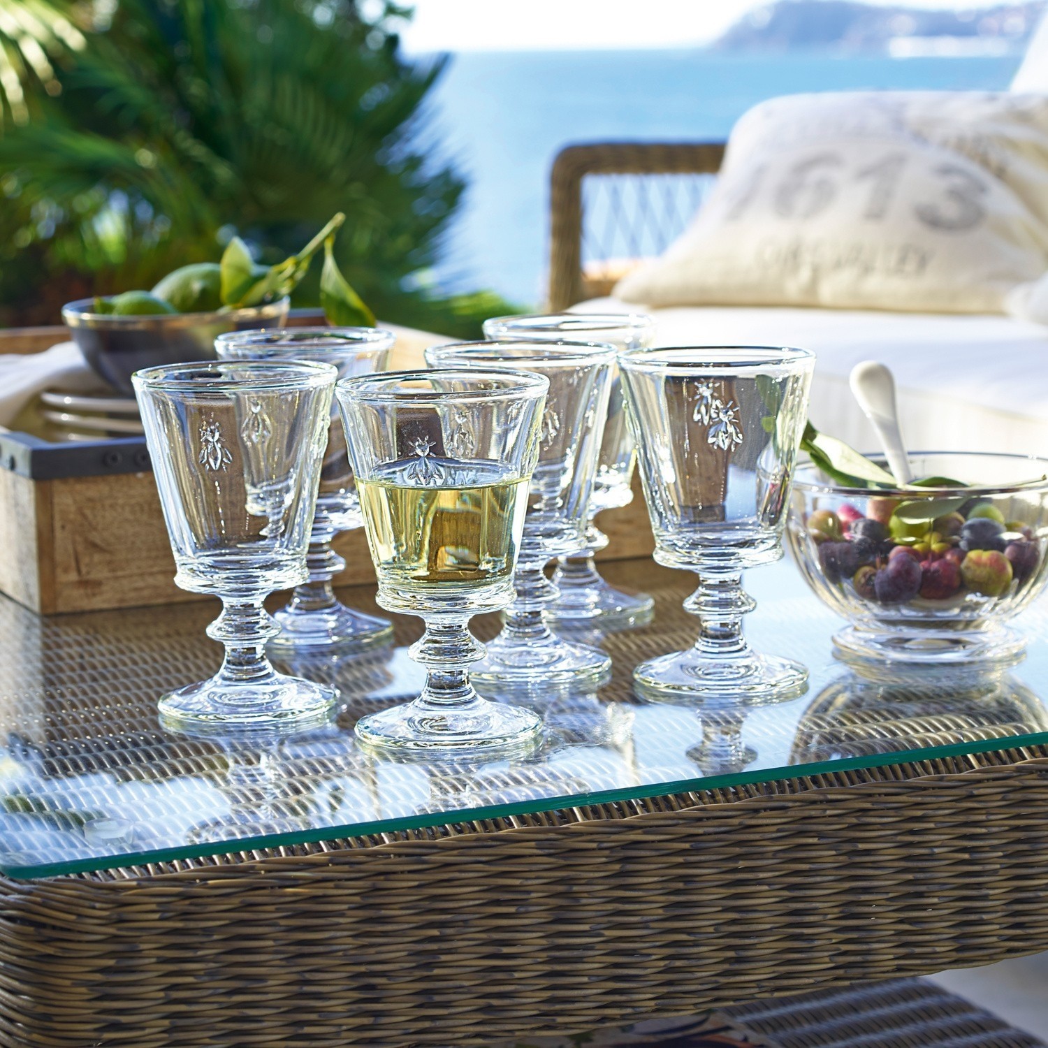 Set van zes glazen met insectmotief op glazen tafel op terras met uitzicht op zee