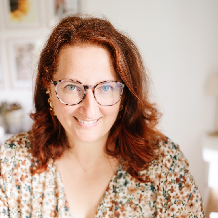 Portret van vrouw met rood haar en bril in bloemenblouse in lichte kamer