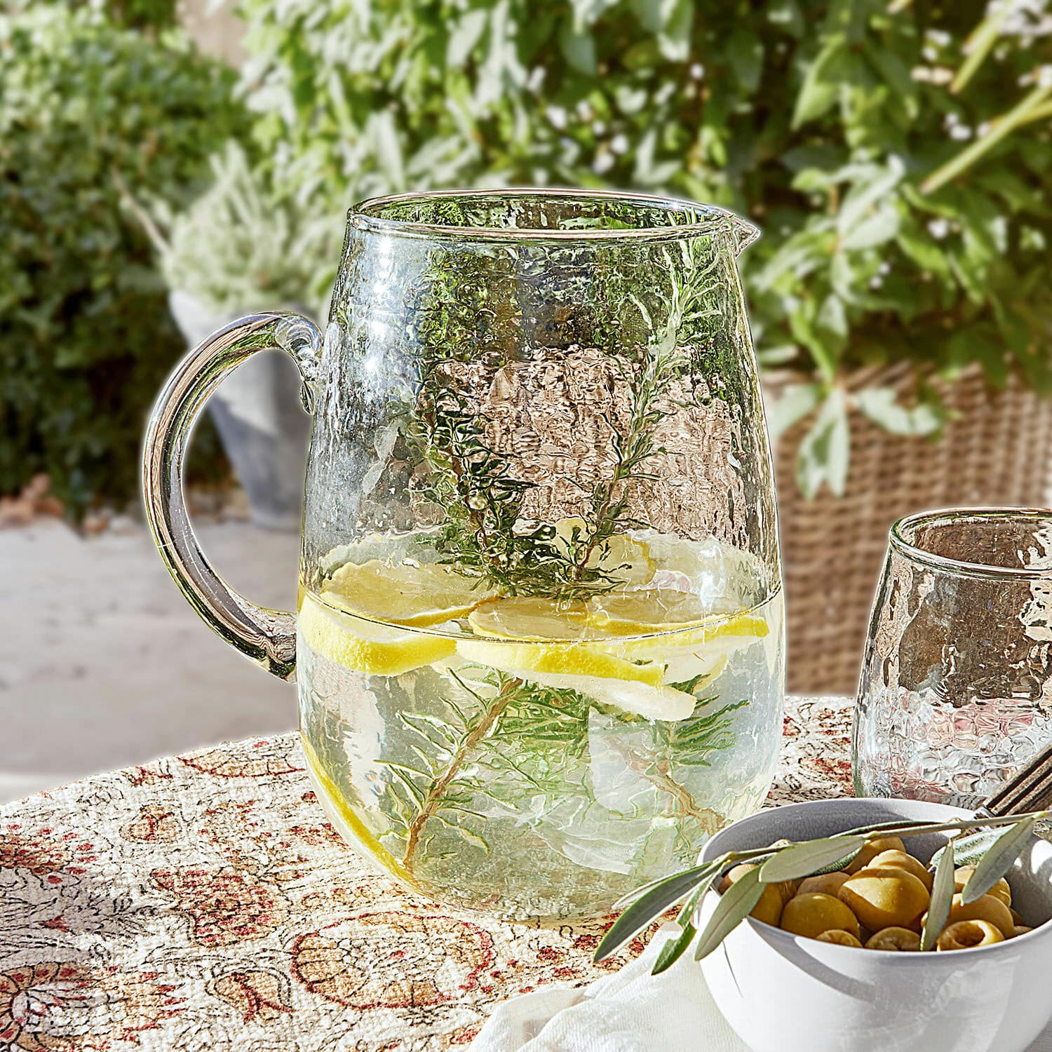 Kan Rezay Glazen kan met water, citroen en kruiden op decoratief tafelkleed, zomerse drank op terras
