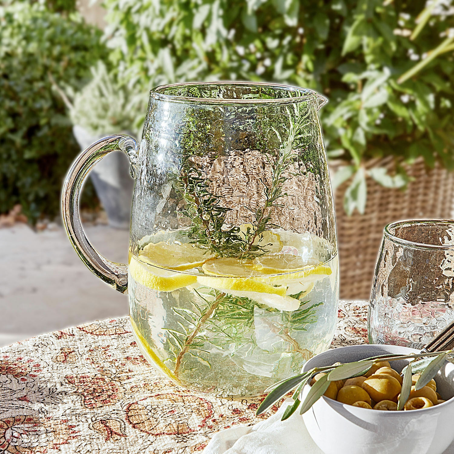 Kan Rezay Glazen kan met water, citroen en kruiden op decoratief tafelkleed, zomerse drank op terras