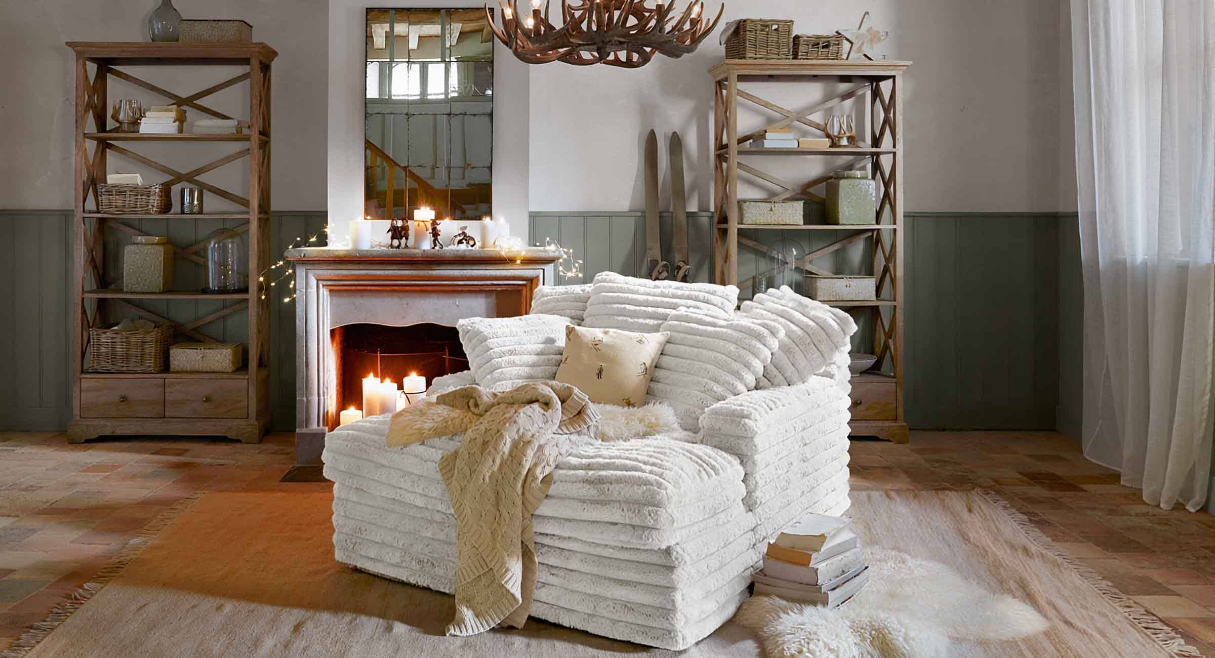 Knusse witte fauteuil van zacht materiaal in chaletstijl met open haard en houten kasten in woonkamer