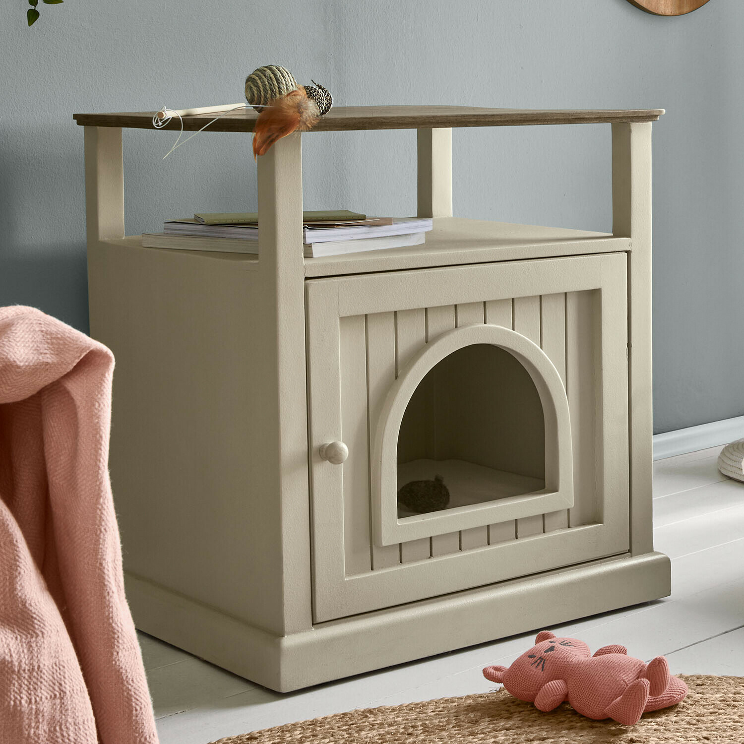 Beige houten kattenhuis met bovenplank, versierd met speelgoed en boeken in een modern interieur