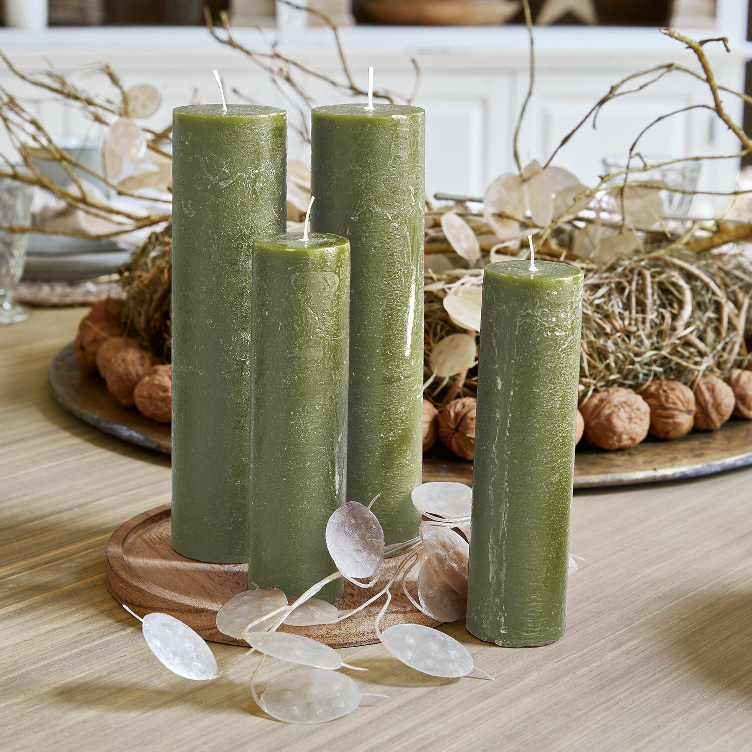 Set van vier groene waskaarsen op houten schaal, natuurlijke tafeldecoratie met takken en noten
