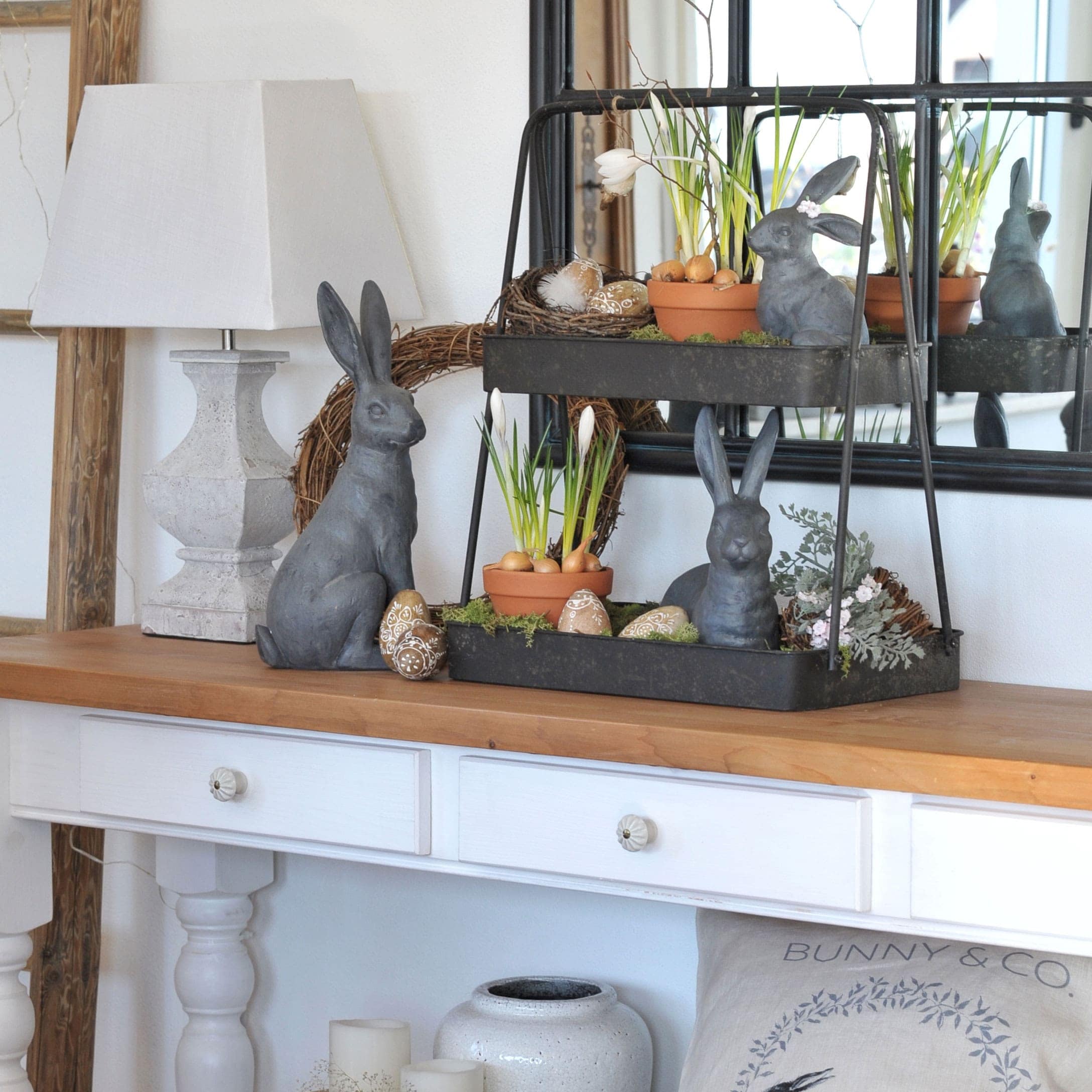 Paasdecoratie met grijze konijnen, bloempotten en versierde eieren op houten tafel