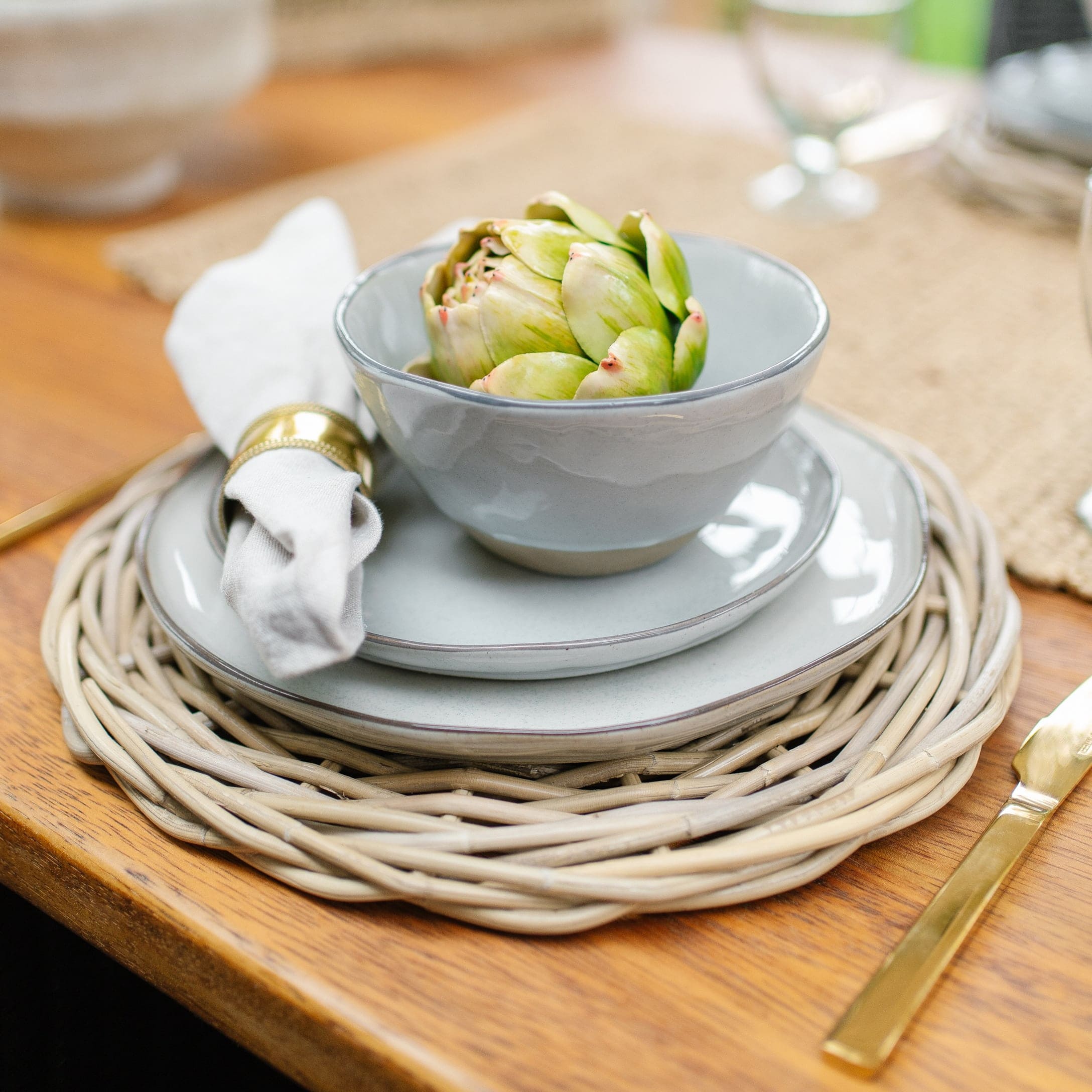 Set grijs keramisch servies op gevlochten onderzetter met groene artisjok en gouden bestek