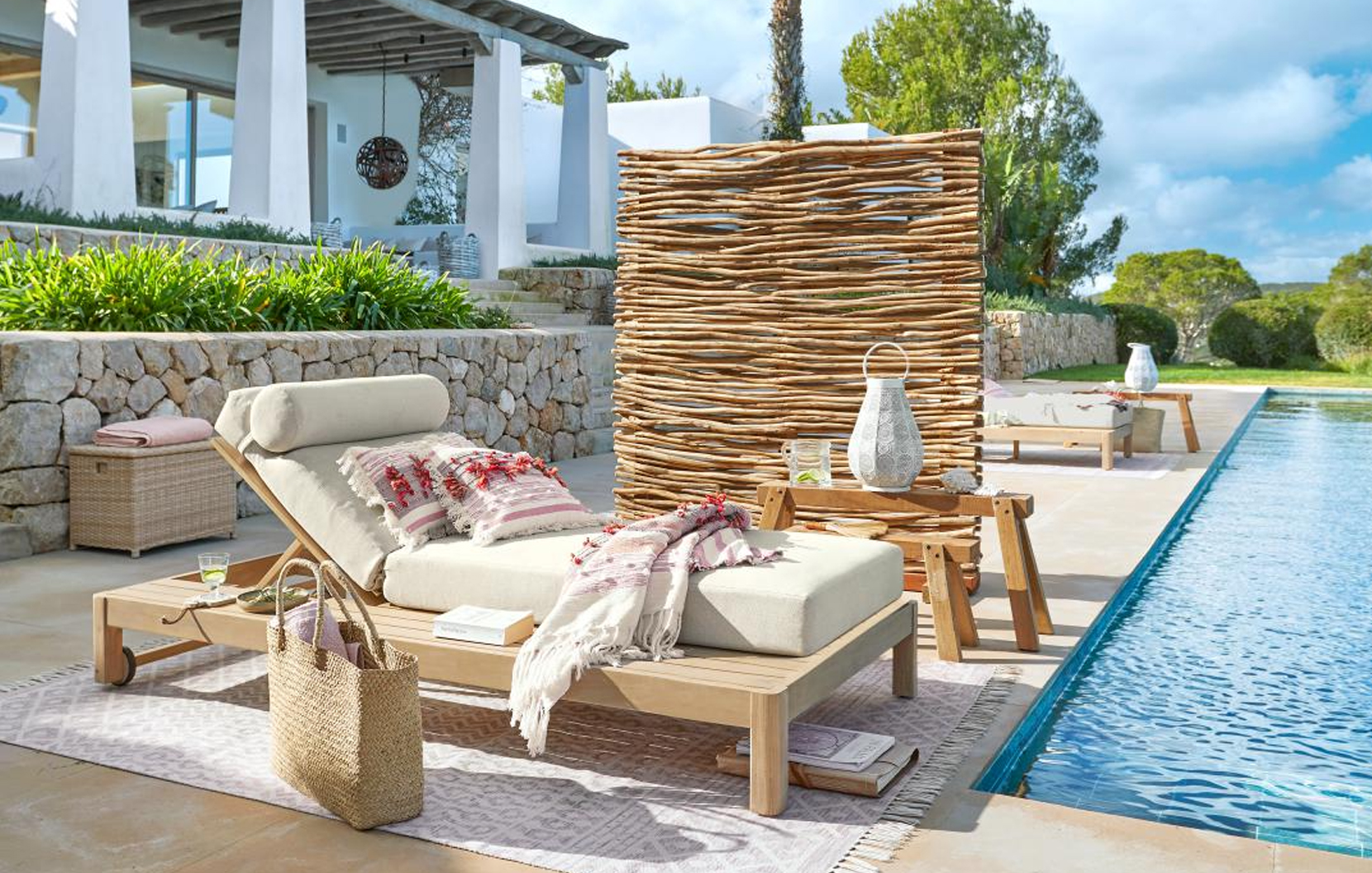 Ligbed van licht hout met crème kussen en decoratief gevlochten scherm bij het zwembad in maritieme stijl