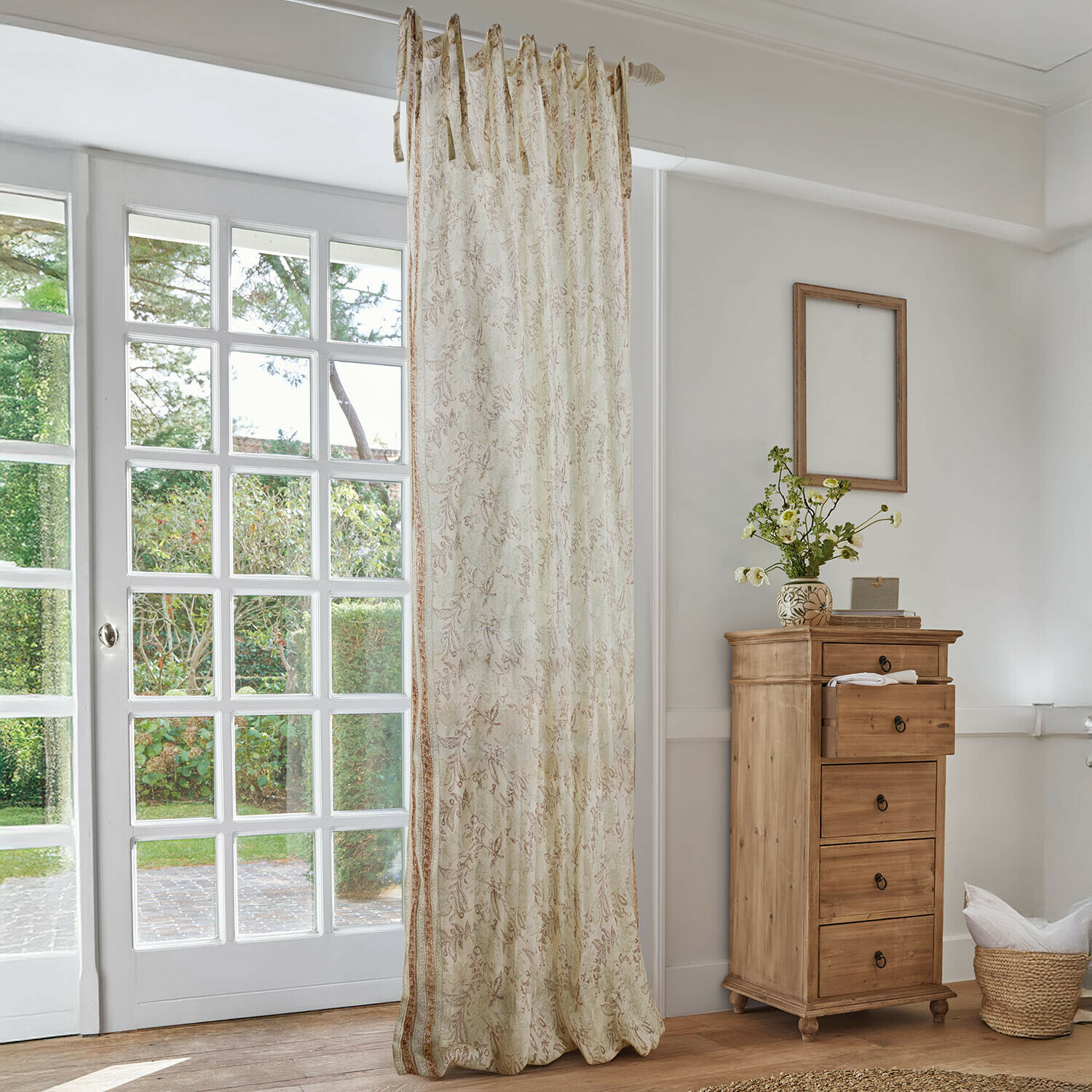 Gordijn Floréane Beige gordijn met fijn bloemmotief in lichte woonkamer met houten ladekast en groot raam