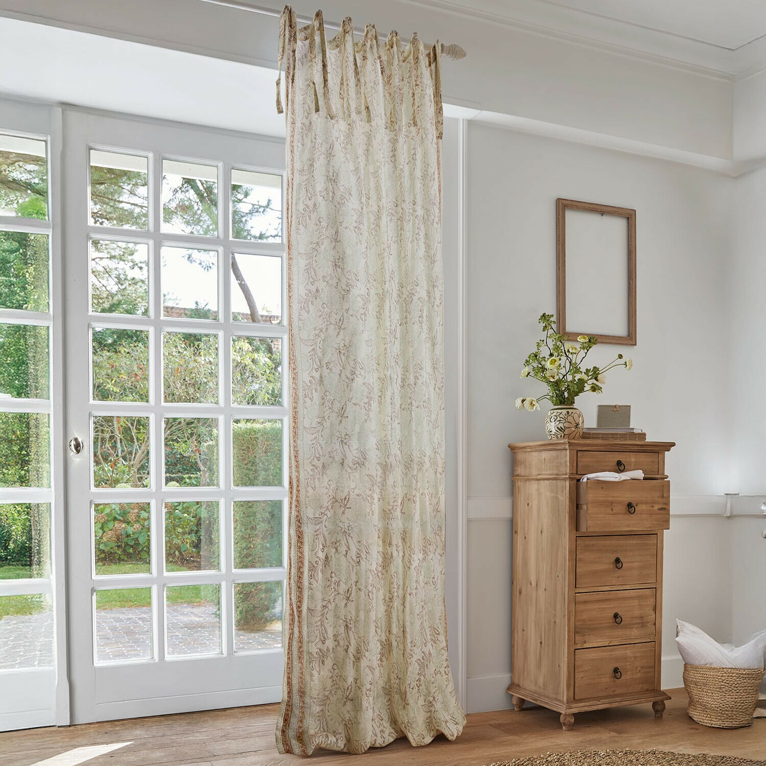 Gordijn Floréane Beige gordijn met fijn bloemmotief in lichte woonkamer met houten ladekast en groot raam