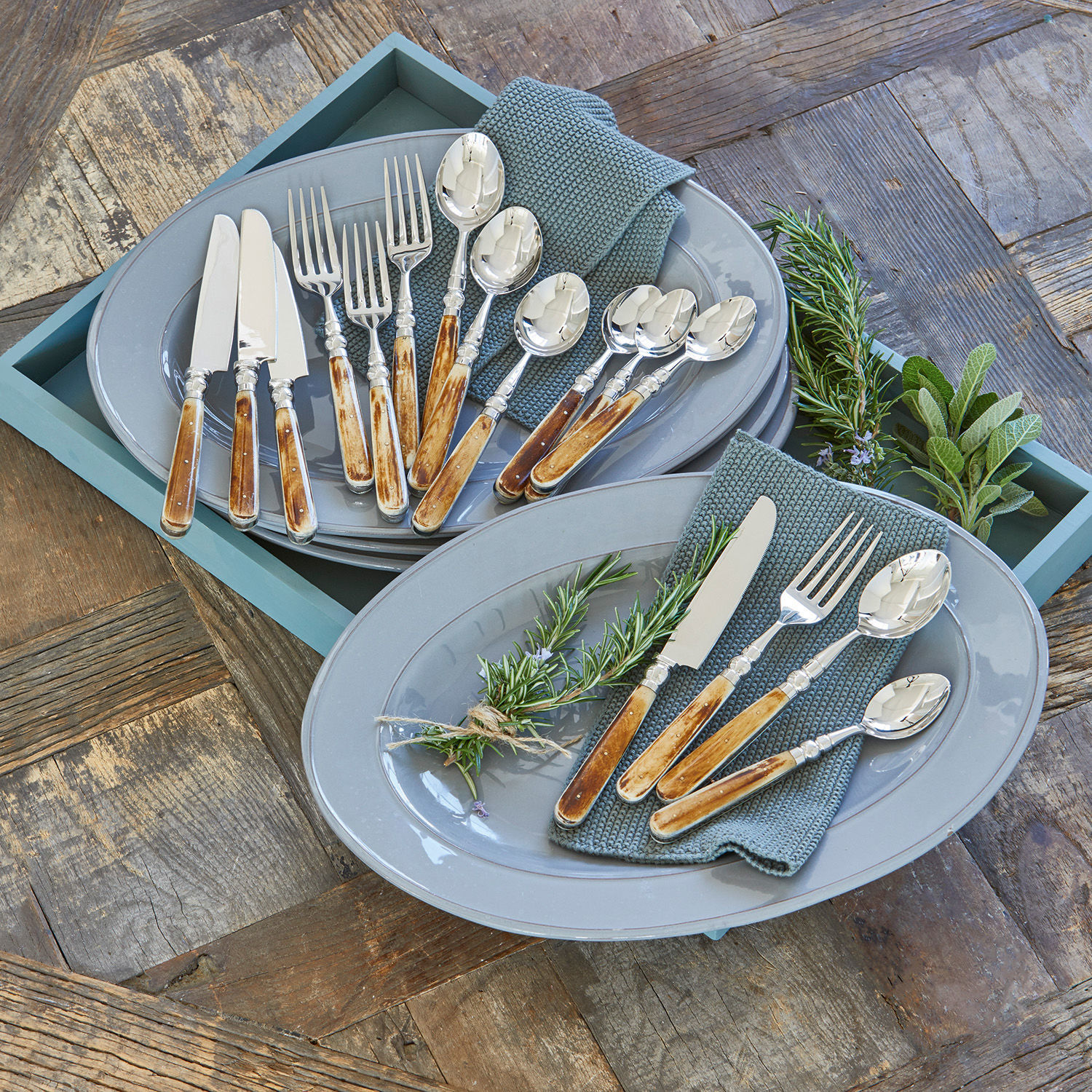Bestekset met houten handvatten op grijze borden met groene servetten en verse kruiden