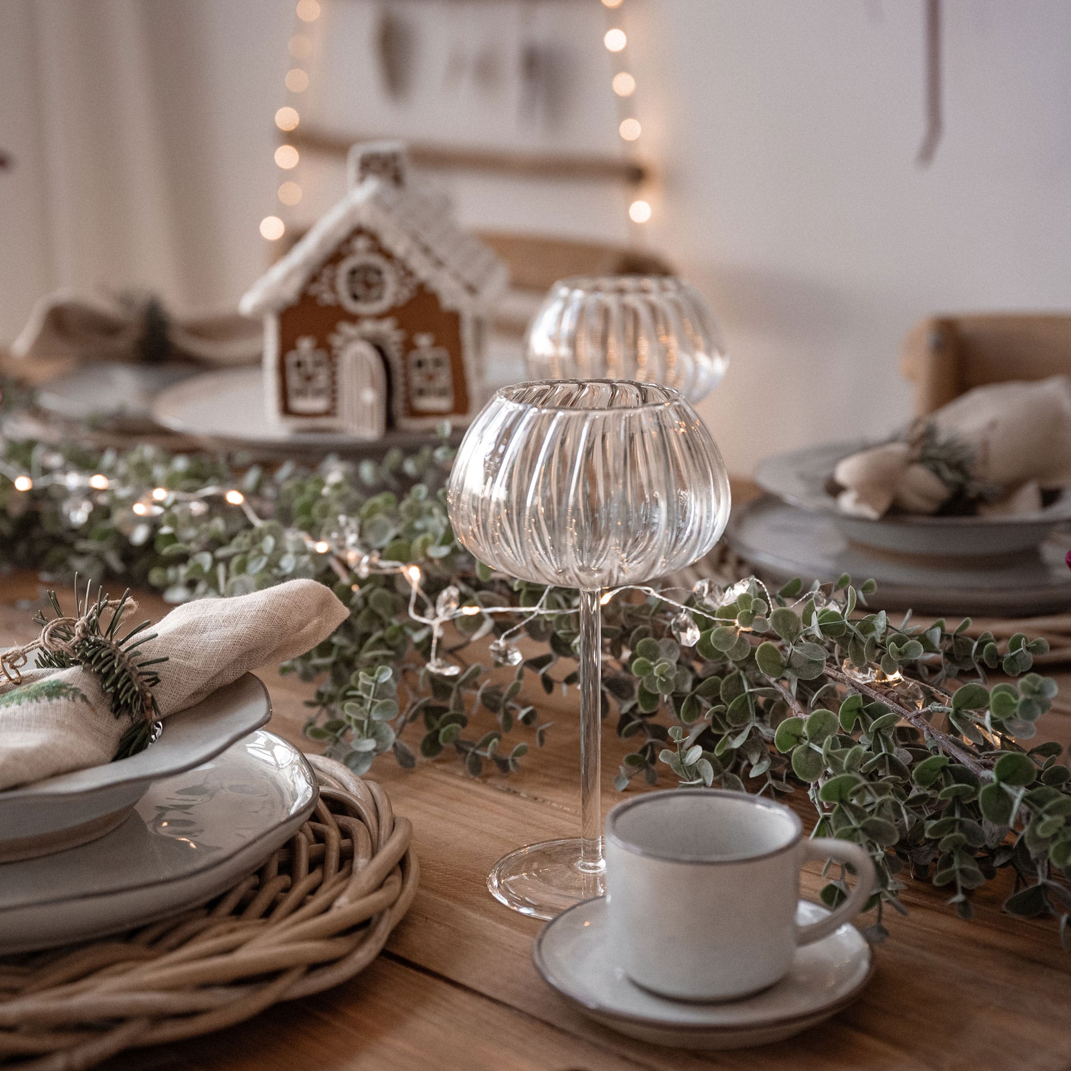 Kersttafel met decoratieve glazen kandelaren, groene takken en witte porseleinen kop