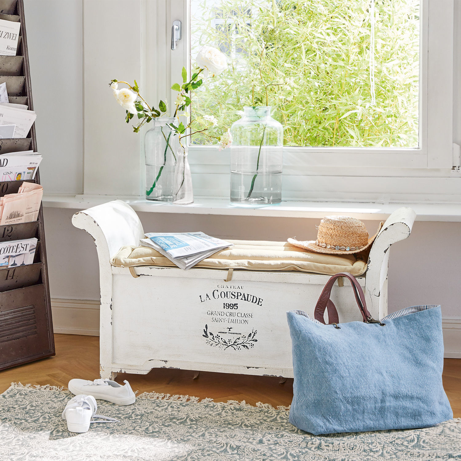 Bank Andance Witte houten bank met kussen, hoed en blauwe tas voor raam met bloemen