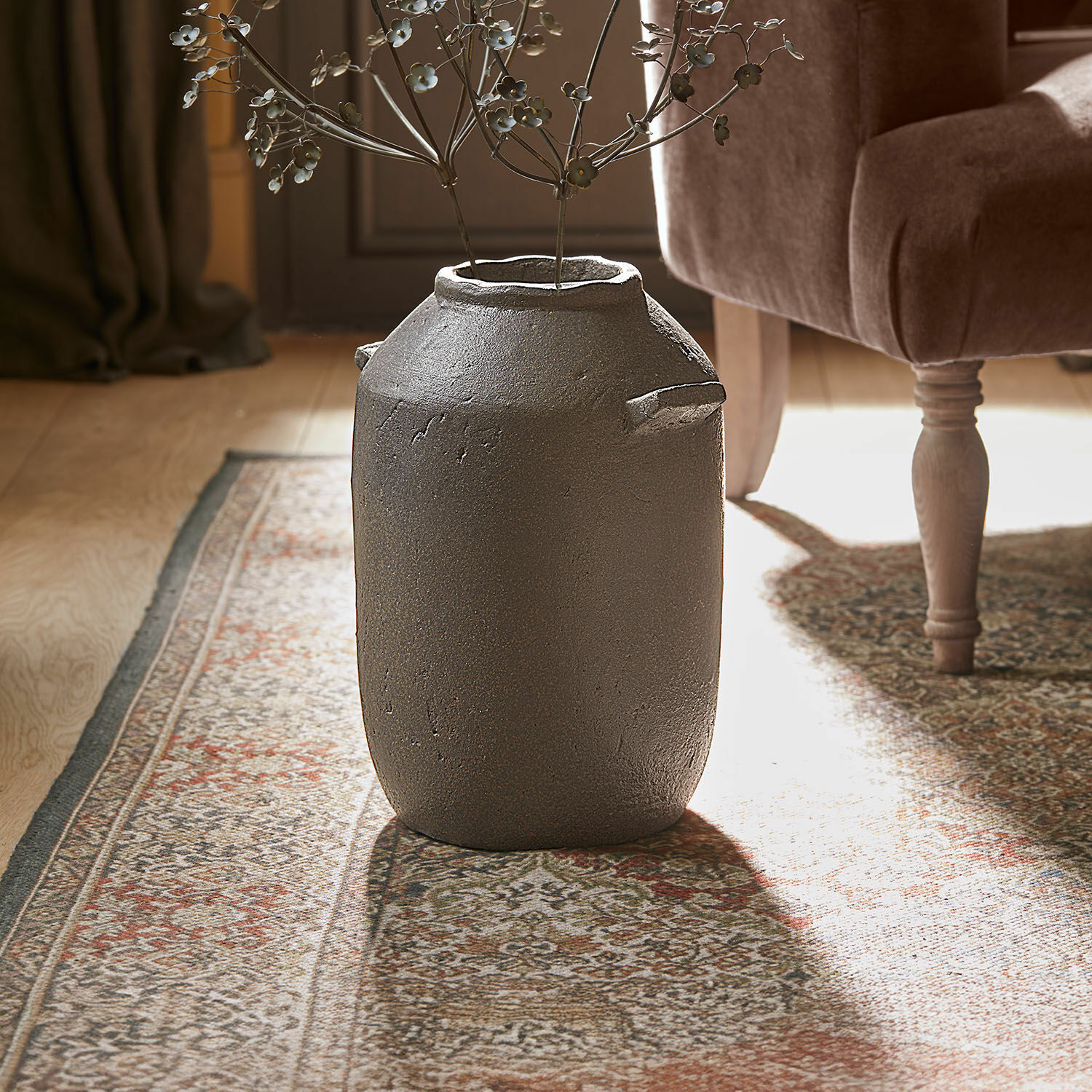 Grote decoratieve vaas van grijs keramiek op tapijt in stijlvolle kamer met metalen bloemen