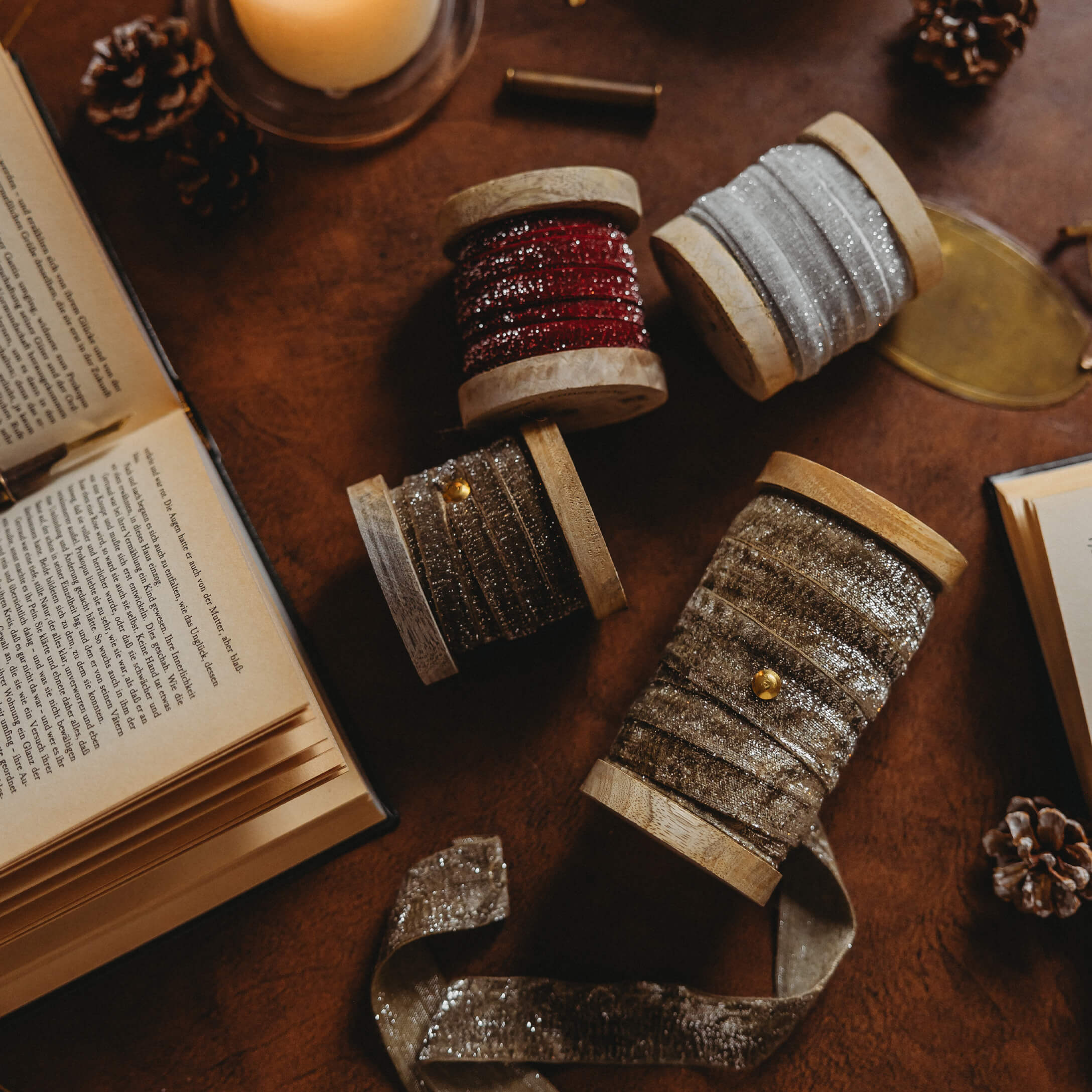 Houten spoelen met glinsterende linten in rood, zilver en goud op tafel met boeken