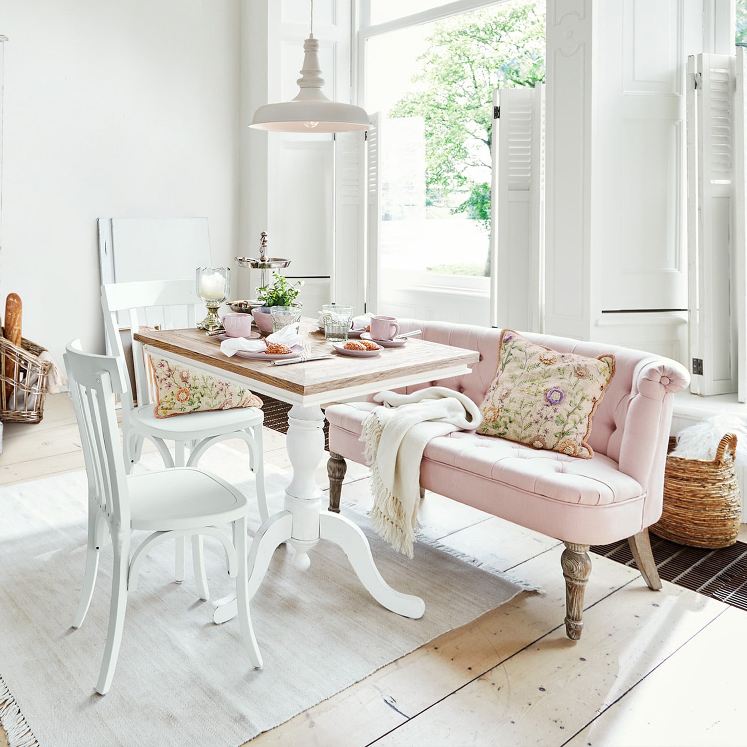 Lichte kamer met witte houten tafel en roze gestoffeerde bank met bloemenkussen
