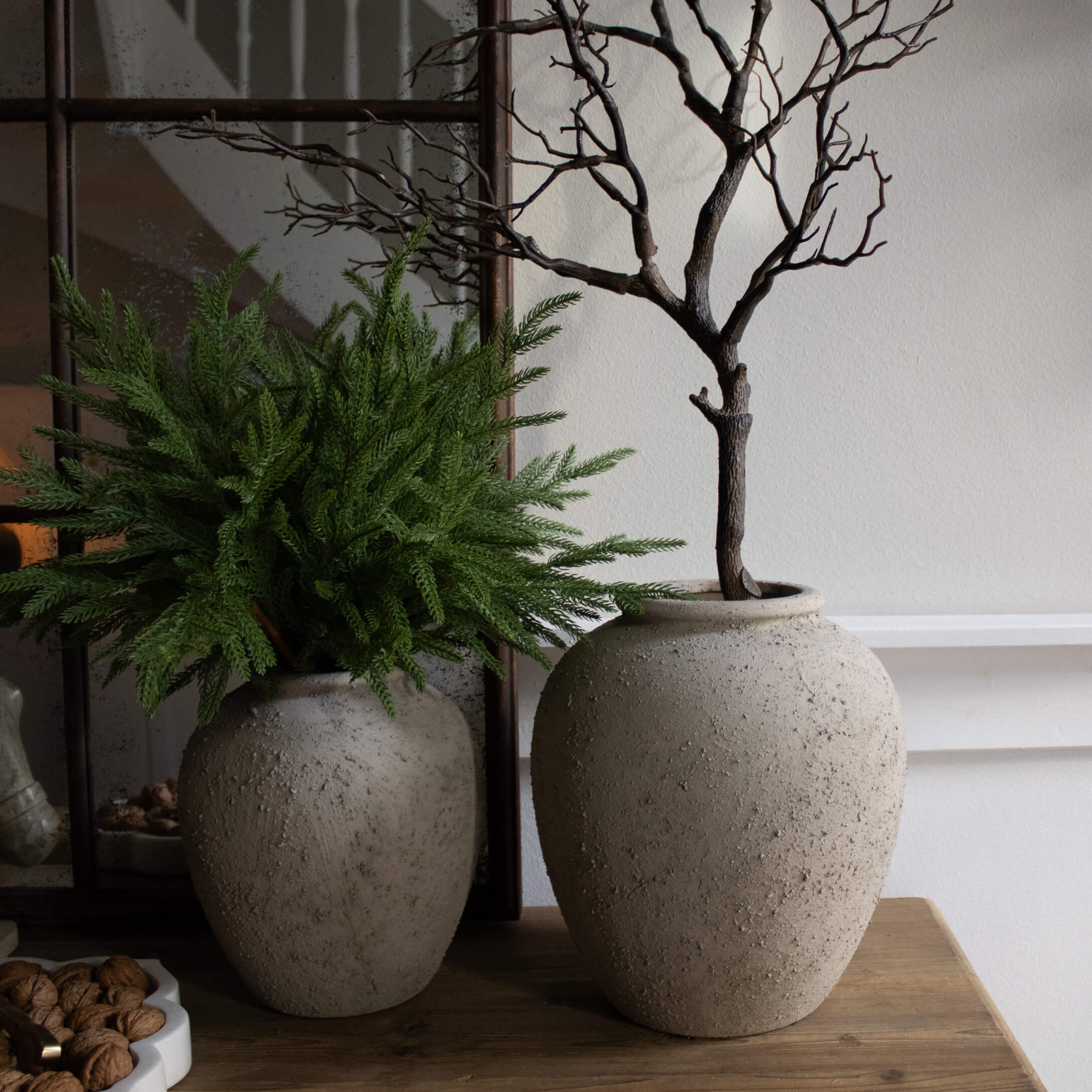 Twee decoratieve grijze stenen vazen op houten tafel met groene en droge takken