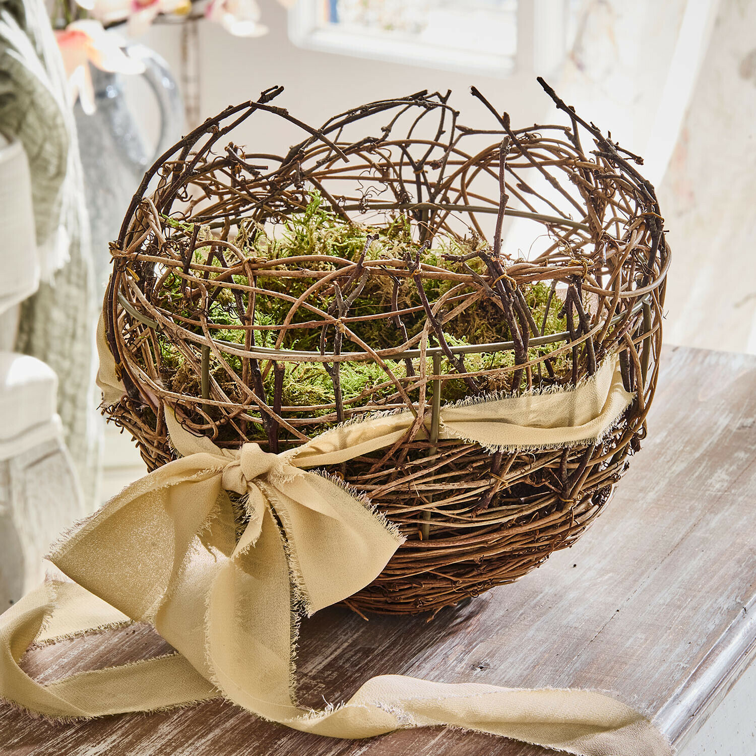 Decoratieve mand van takken met groen mos en beige lint op houten tafel voor interieurdecoratie