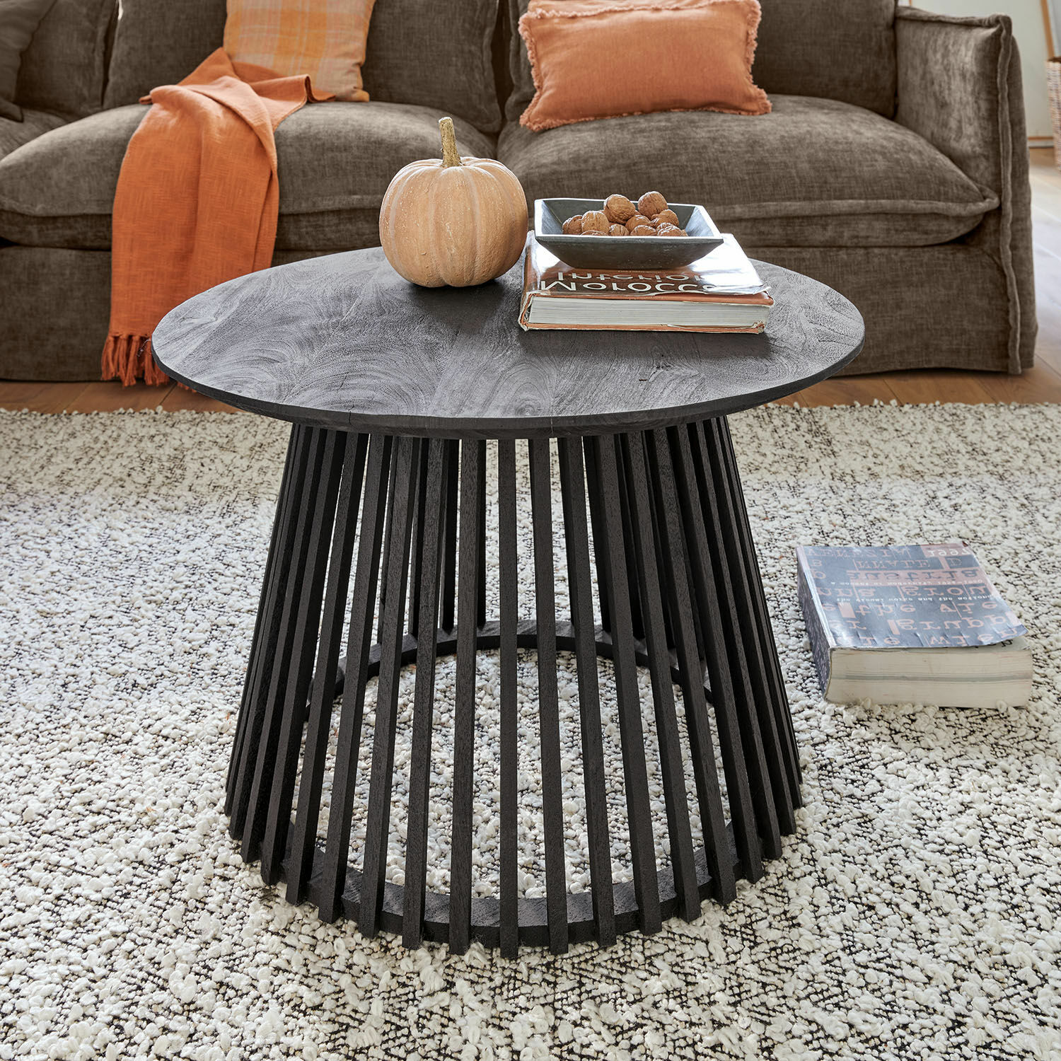 Ronde zwarte salontafel van mangohout met open onderstel op lichte vloerkleed in woonkamer