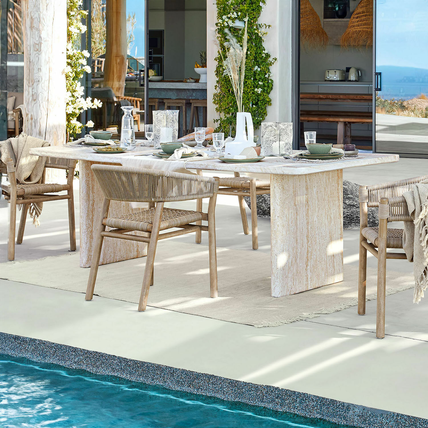 Eettafel Yveline Eettafel van lichte steen met houten stoelen en gevlochten rugleuning bij zwembad in modern huis