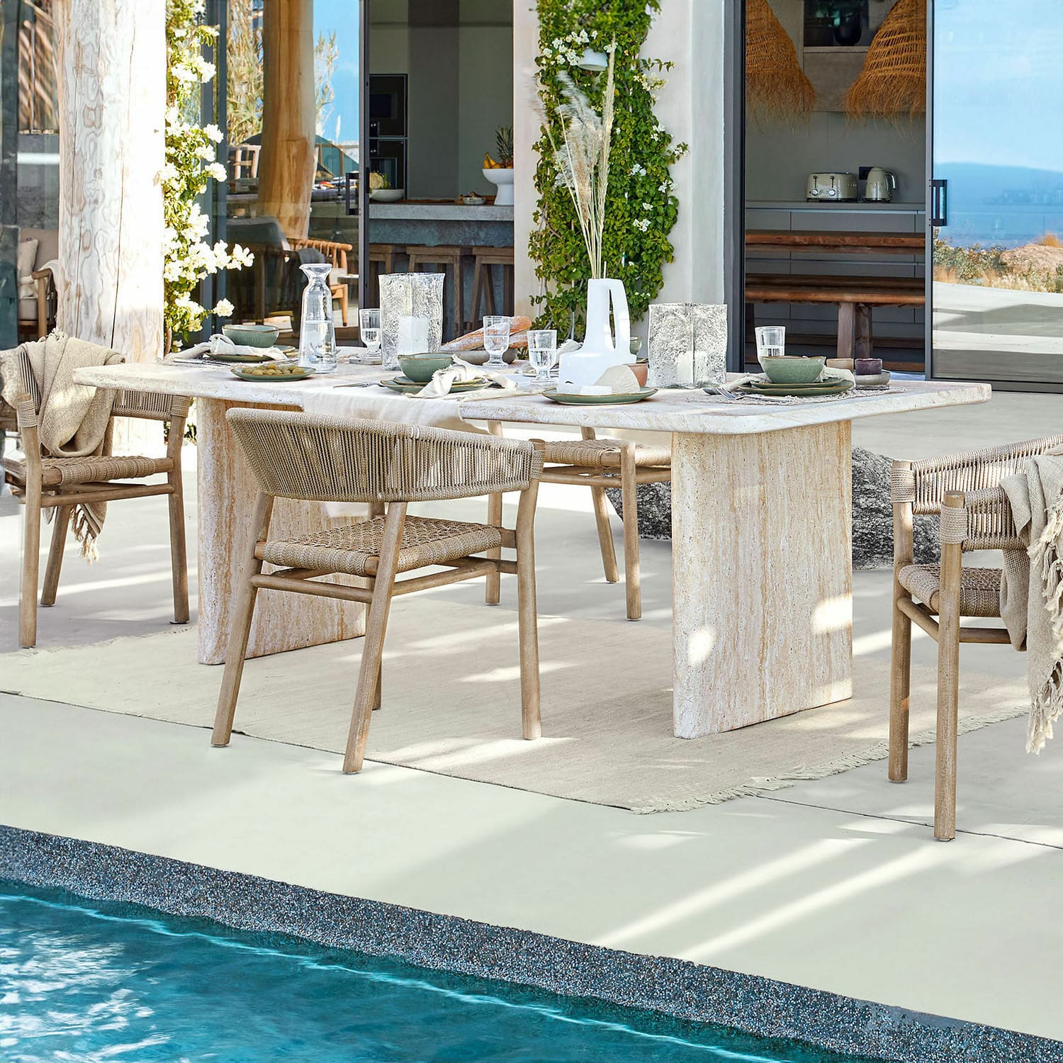 Eettafel Yveline Eettafel van lichte steen met houten stoelen en gevlochten rugleuning bij zwembad in modern huis