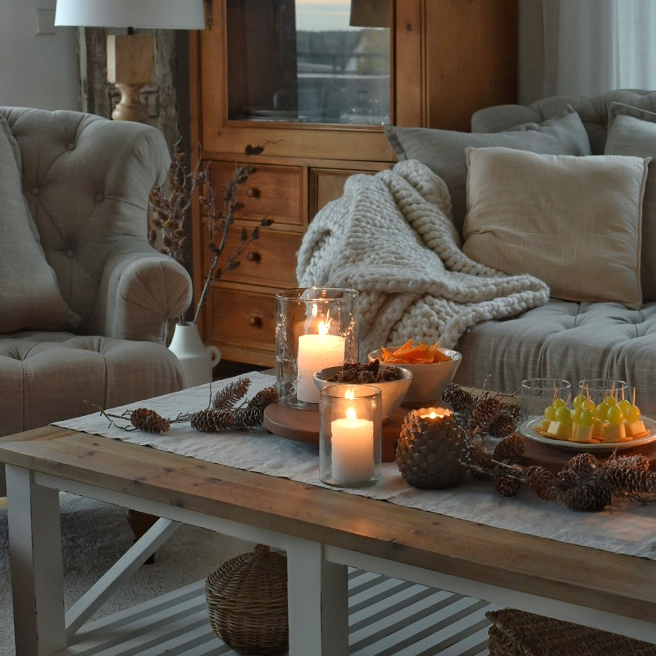 Gezellige woonkamer met houten tafel, brandende kaarsen en grijze zachte deken op bank