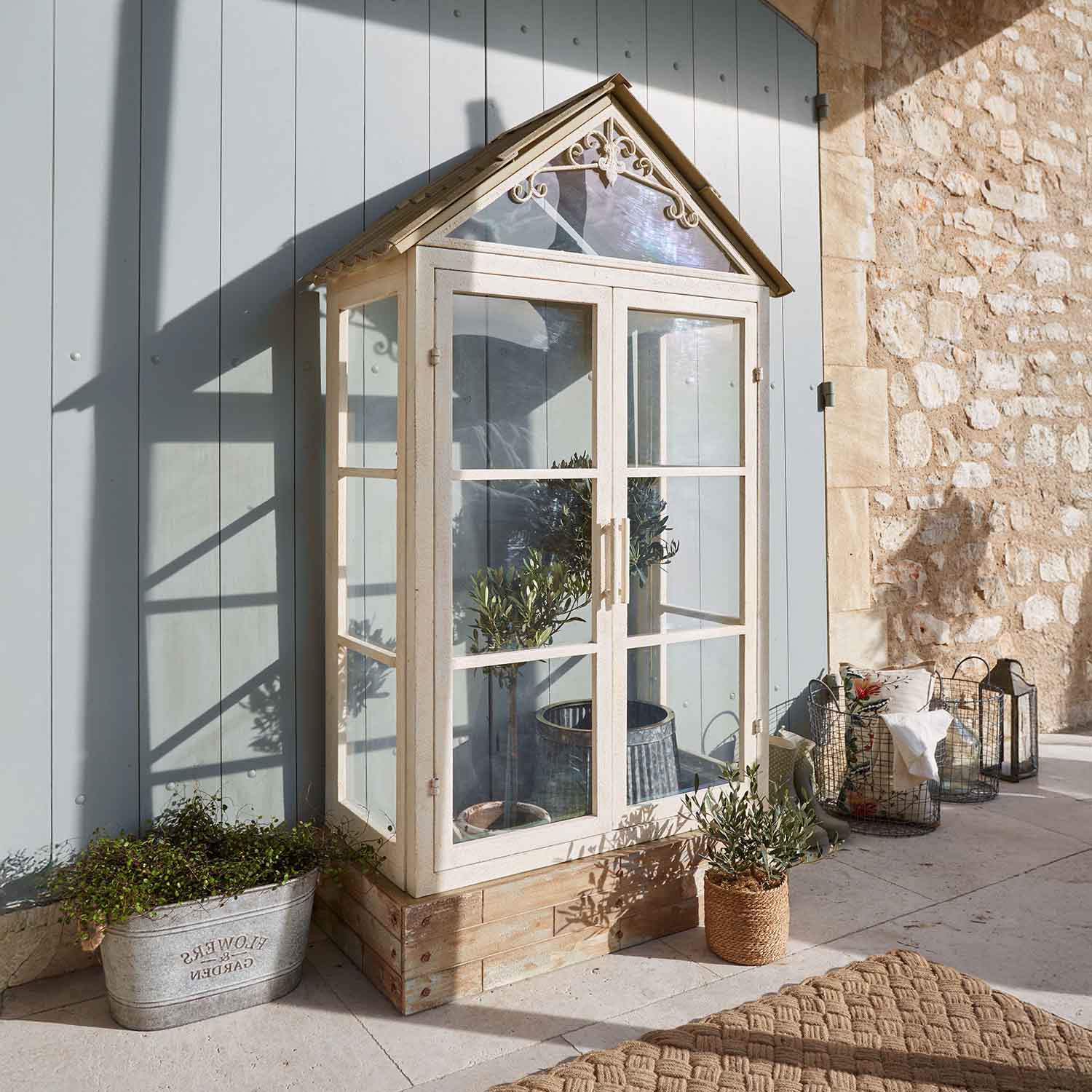Kleine kas van metaal en glas in crèmekleur met planten, terrasdecoratie