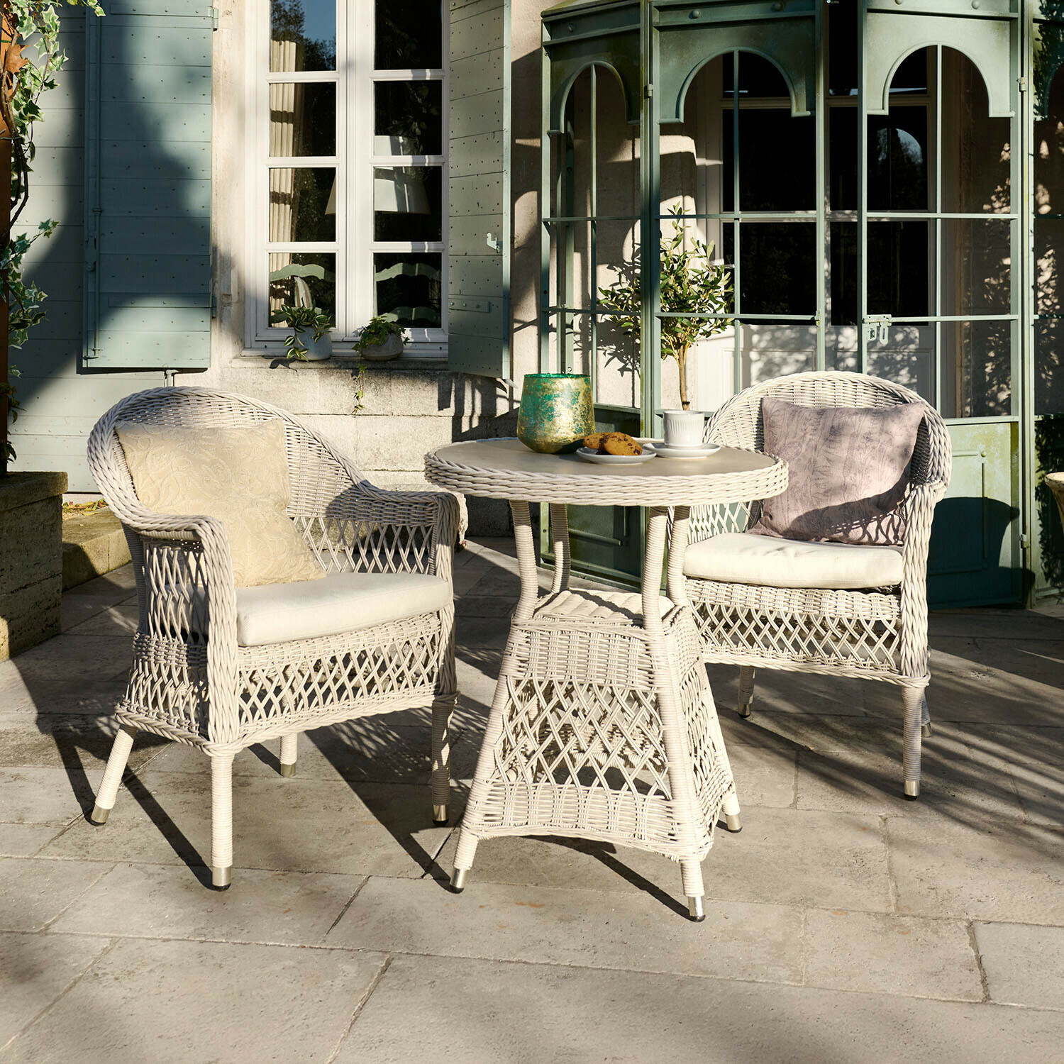 Witte rotan tuinmeubelset met kussens, ronde tafel en twee stoelen op terras