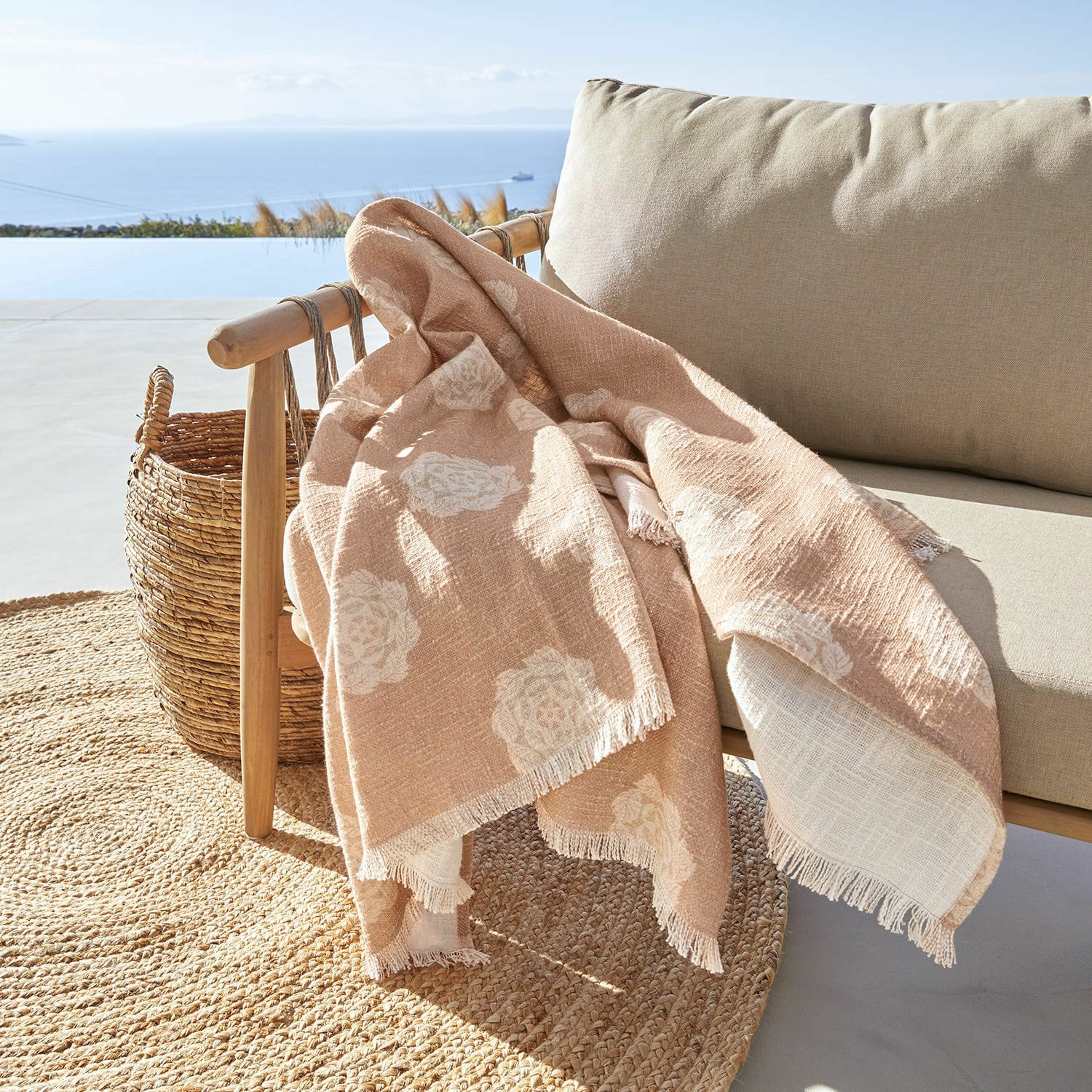 Plaid Belvienne Beige deken met wit bloemenpatroon van zachte stof op houten stoel op terras met zeezicht