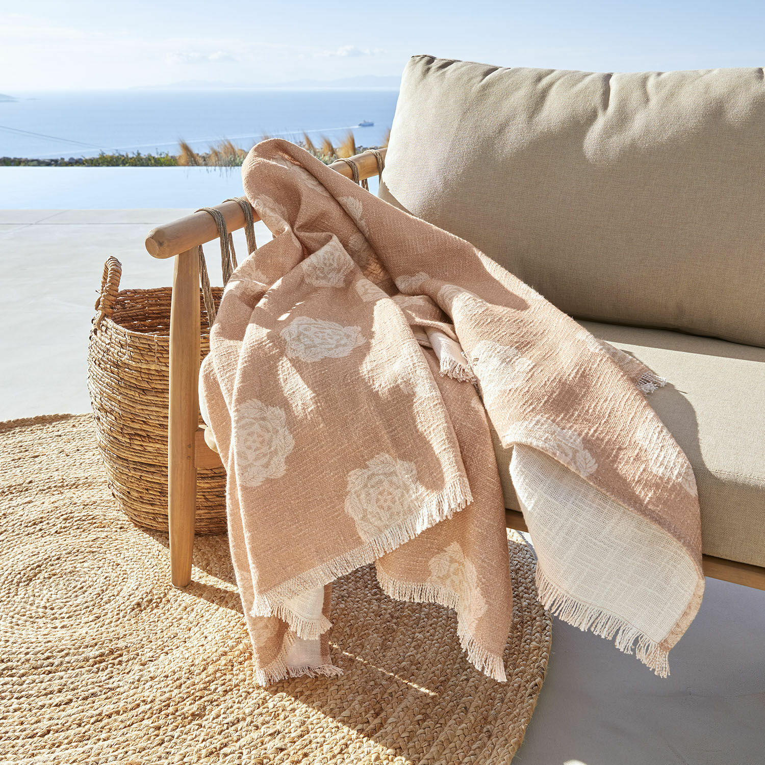 Plaid Belvienne Beige deken met wit bloemenpatroon van zachte stof op houten stoel op terras met zeezicht
