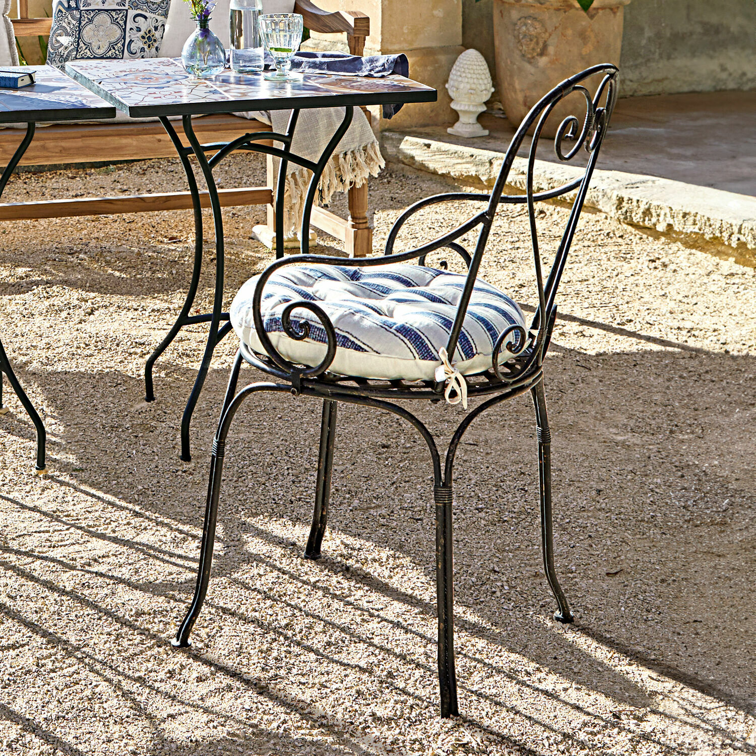 Metalen tuinstoel met blauw-wit gestreept kussen op zonnig terras met grindvloer