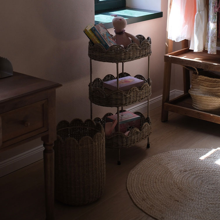 Drie verdiepingen hoge rek van natuurlijke riet met boeken en speelgoed in een gezellige kamer