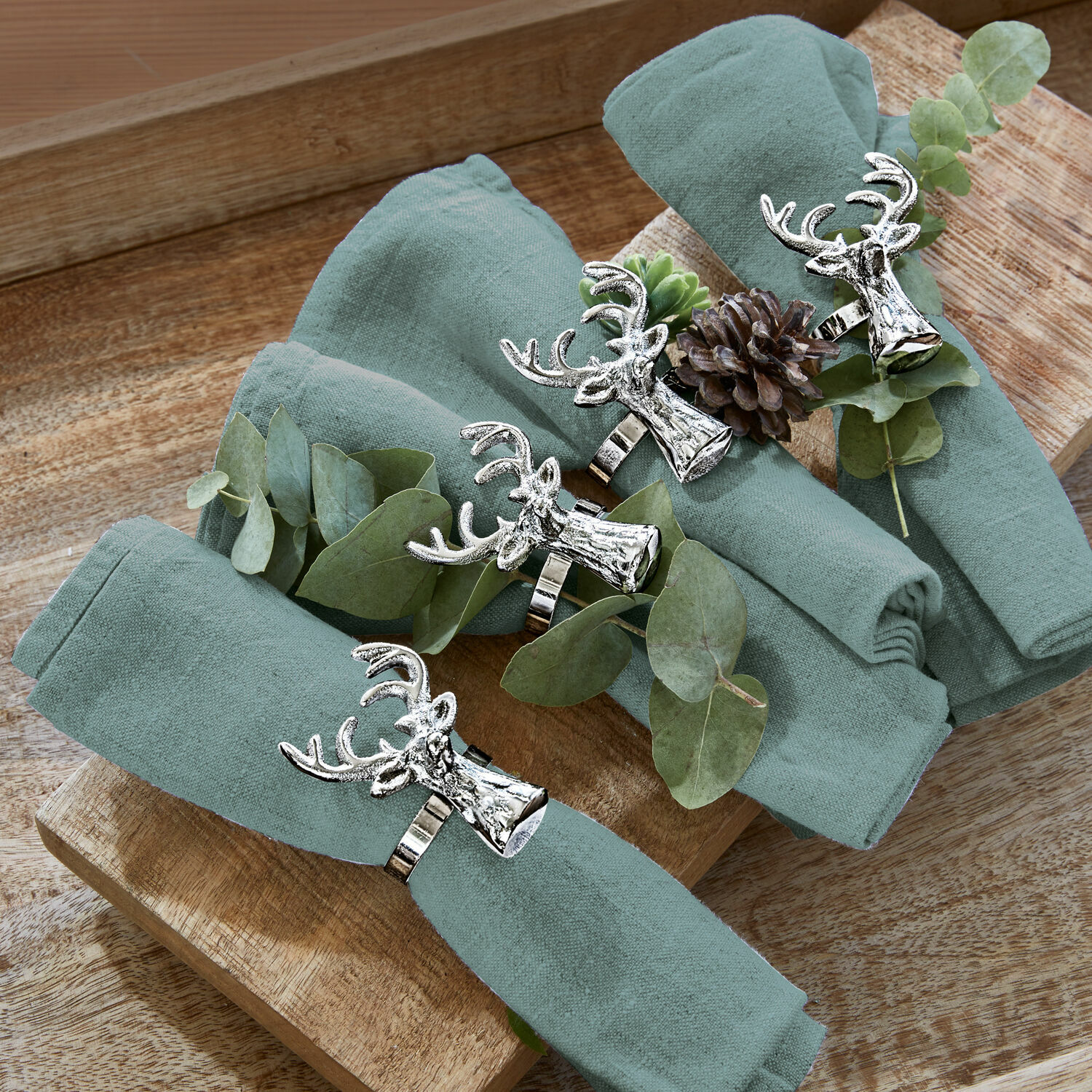 Set van vier groene linnen servetten met metalen servetringen in hertenkopvorm op houten dienblad