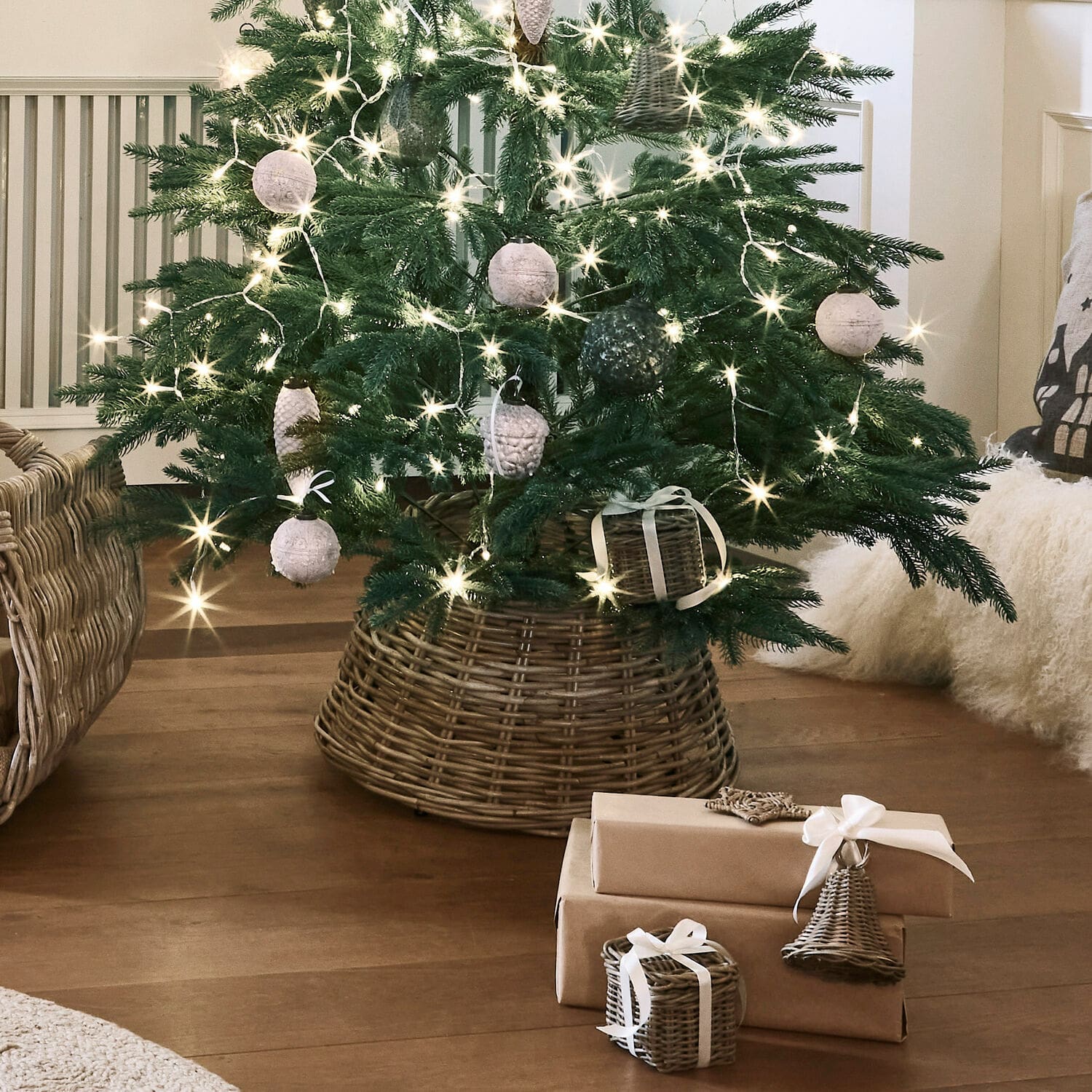 Mand voor kerstboomvoet Kiente Kerstboom in een rieten standaard met natuurlijke versieringen en cadeaus in bruin papier op een houten vloer