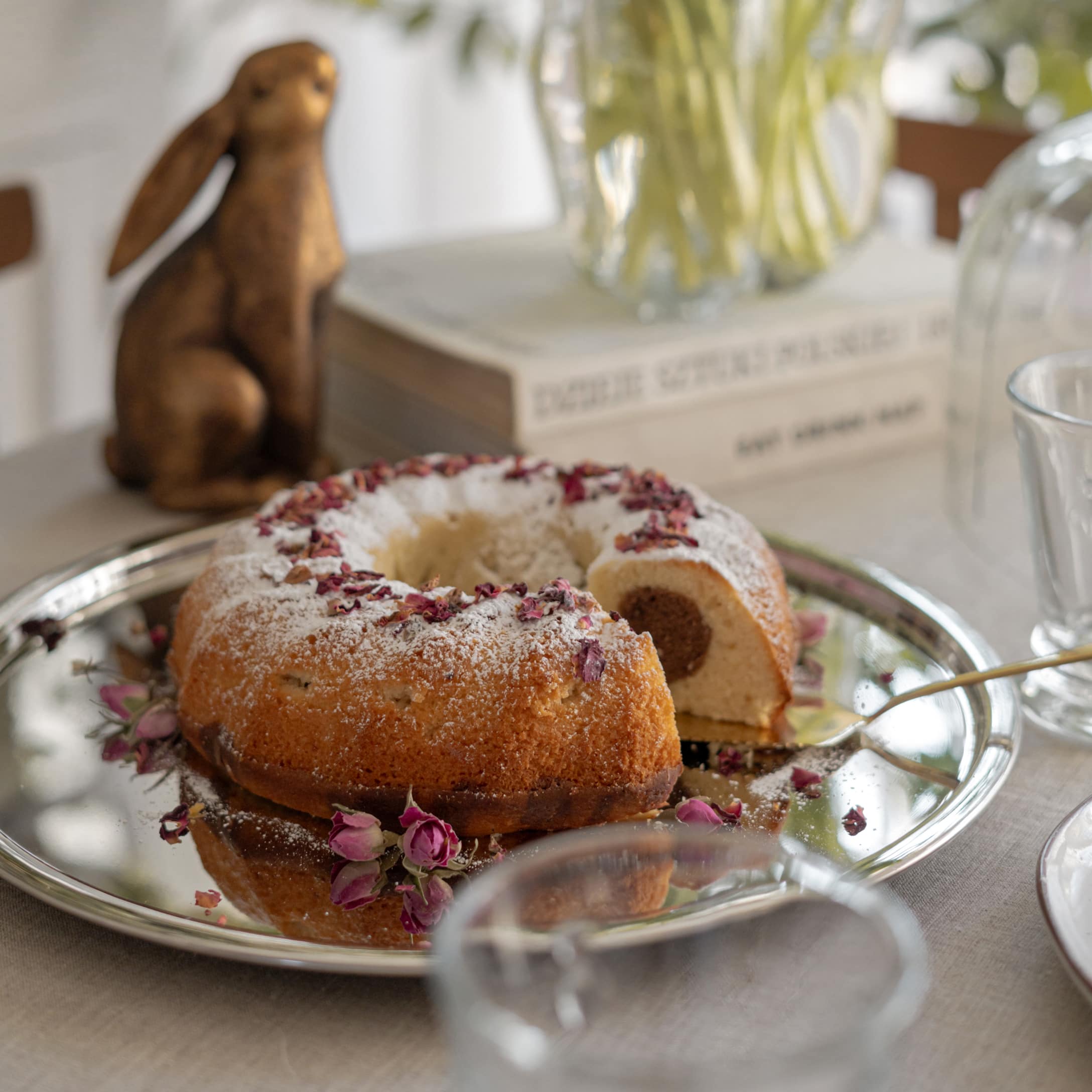 Kransvormige cake met poedersuiker en gedroogde rozenblaadjes op zilveren schaal op tafel