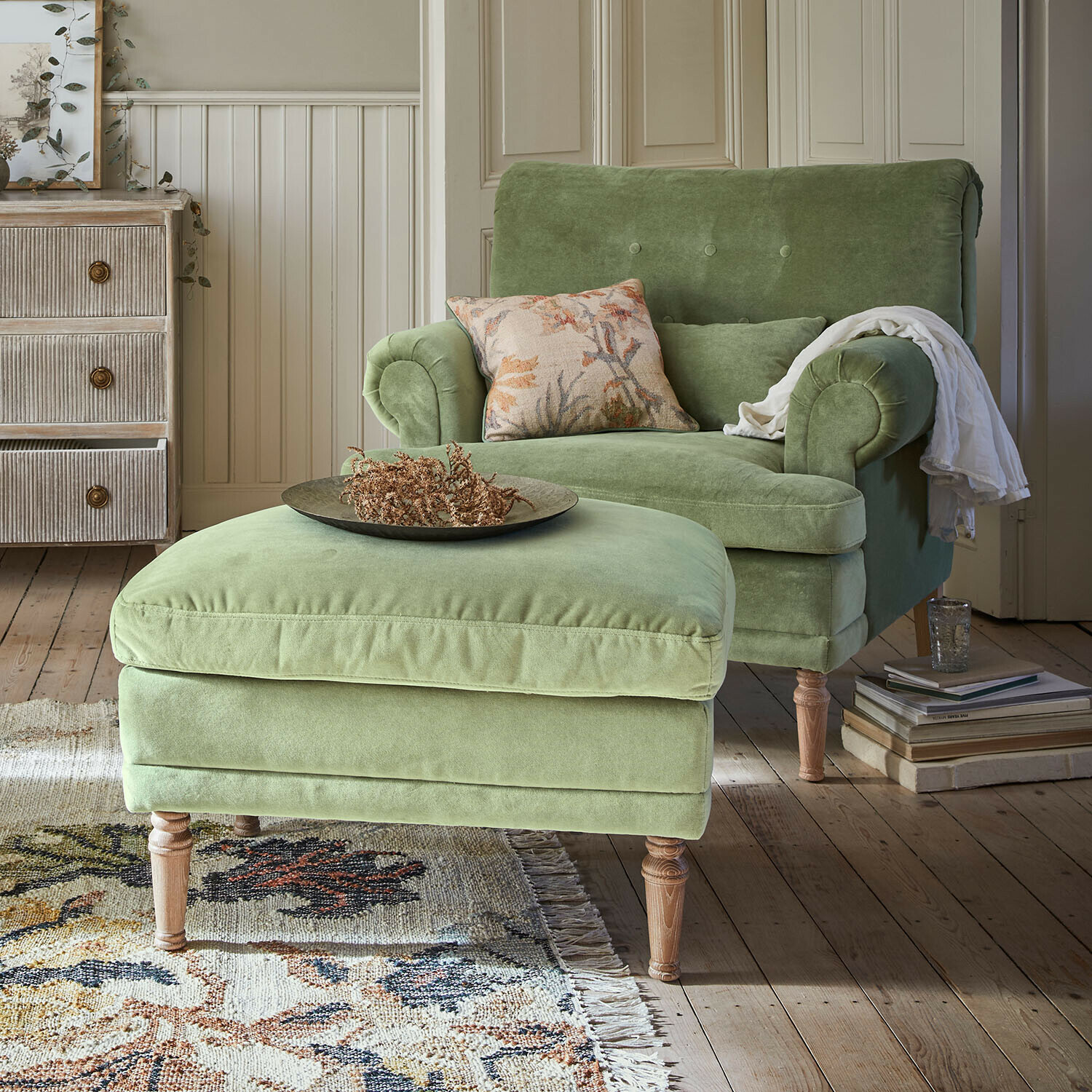 Groene fluwelen fauteuil met voetenbank op houten poten in gezellige woonkamer met vloerkleed