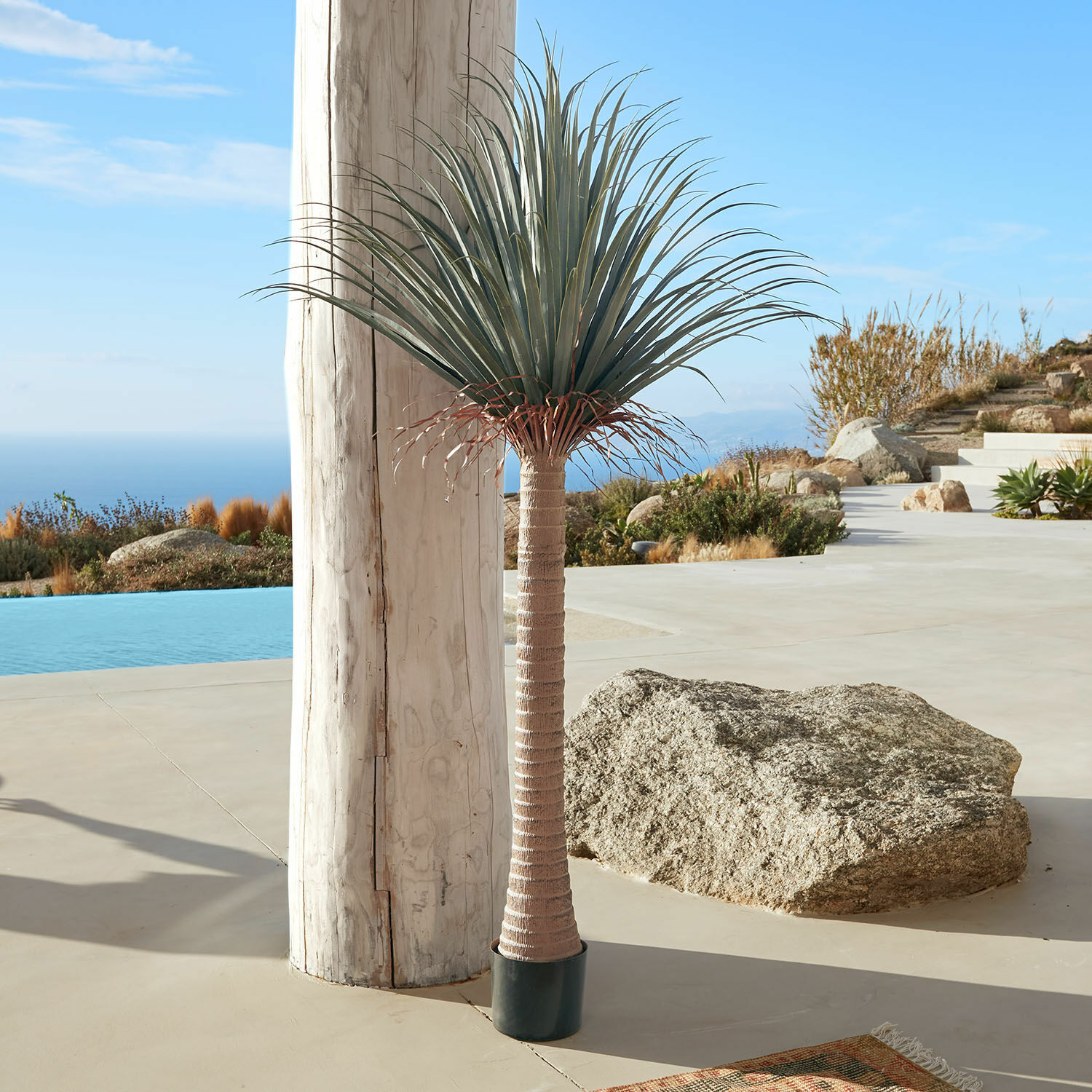 Decoratieve palmboom Remivon Kunstpalm in pot met bruine stam en groene bladeren op terras met zeezicht