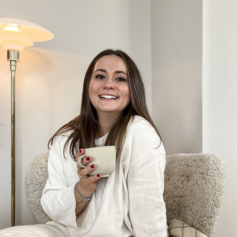 Lachende vrouw in witte trui met beige mok zittend in zachte stoel in lichte kamer