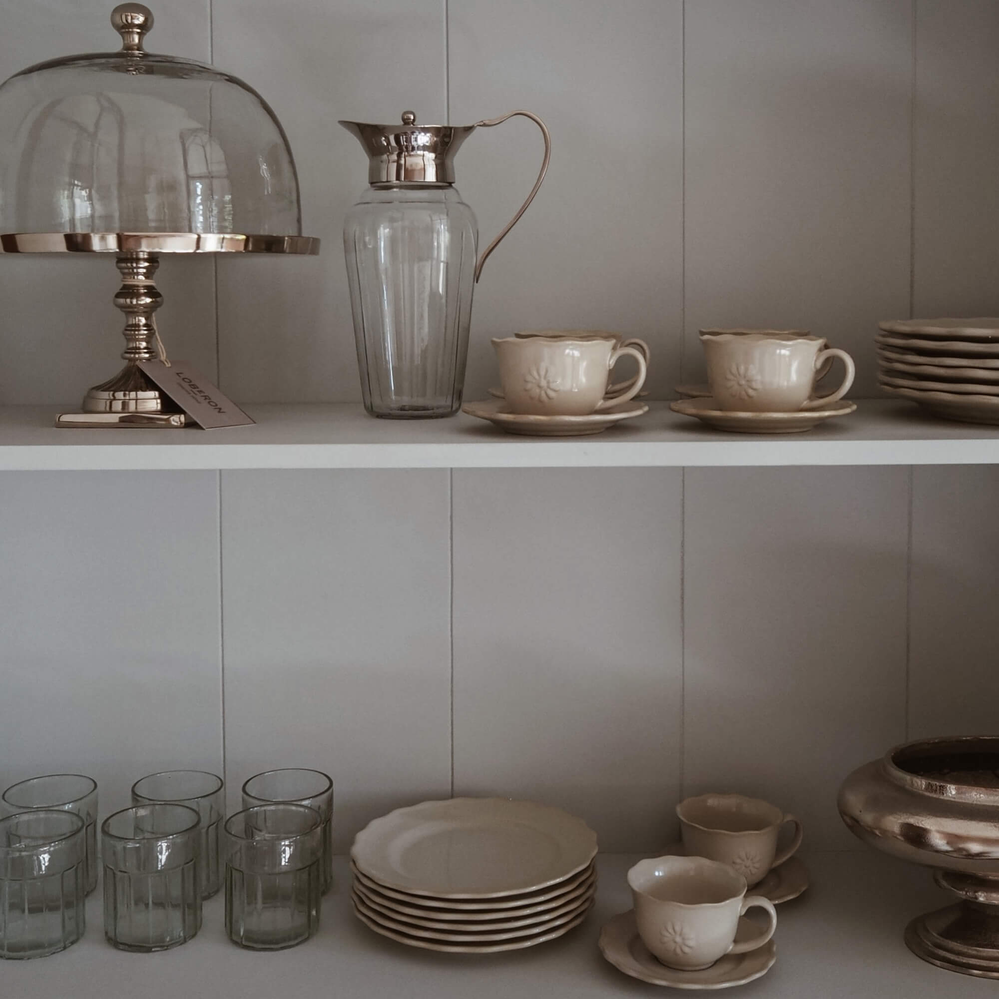 Set crème keramiek met kopjes en borden, glazen kan met metalen handvat op plank