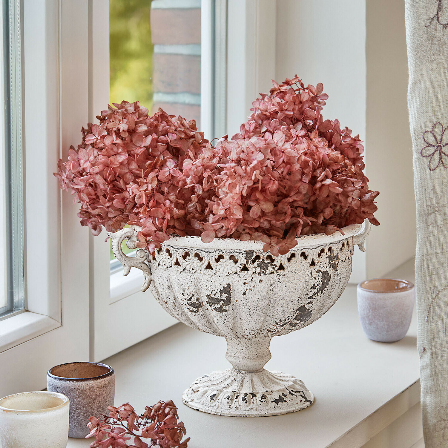 Witte metalen schaal met verweerd oppervlak en gedroogde roze bloemen op vensterbank