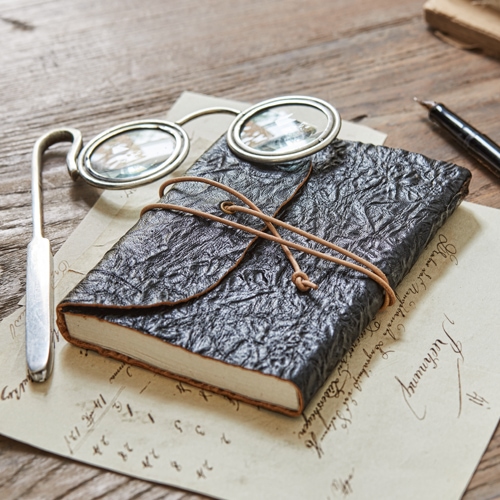 Zwart notitieboek van getextureerd leer met koordsluiting op houten tafel met bril en pen
